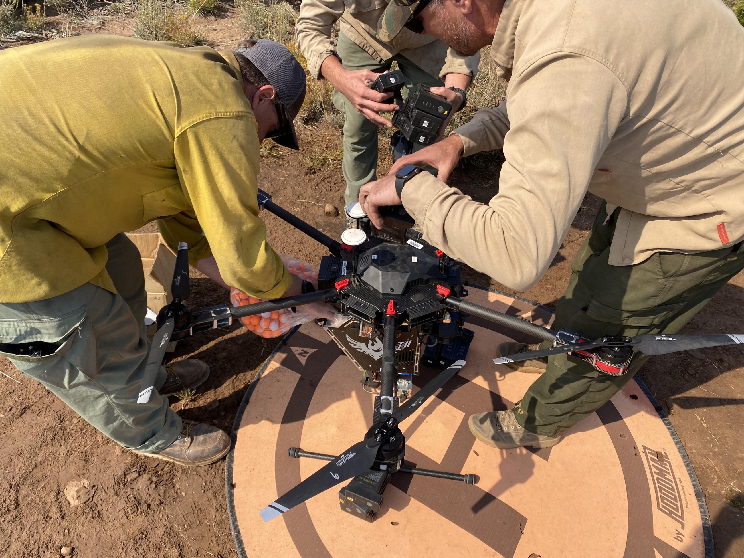Image of firefighters reloading the UAS drone for aerial ignition operations, changing batteries and adding dragon eyes to hopper basket.