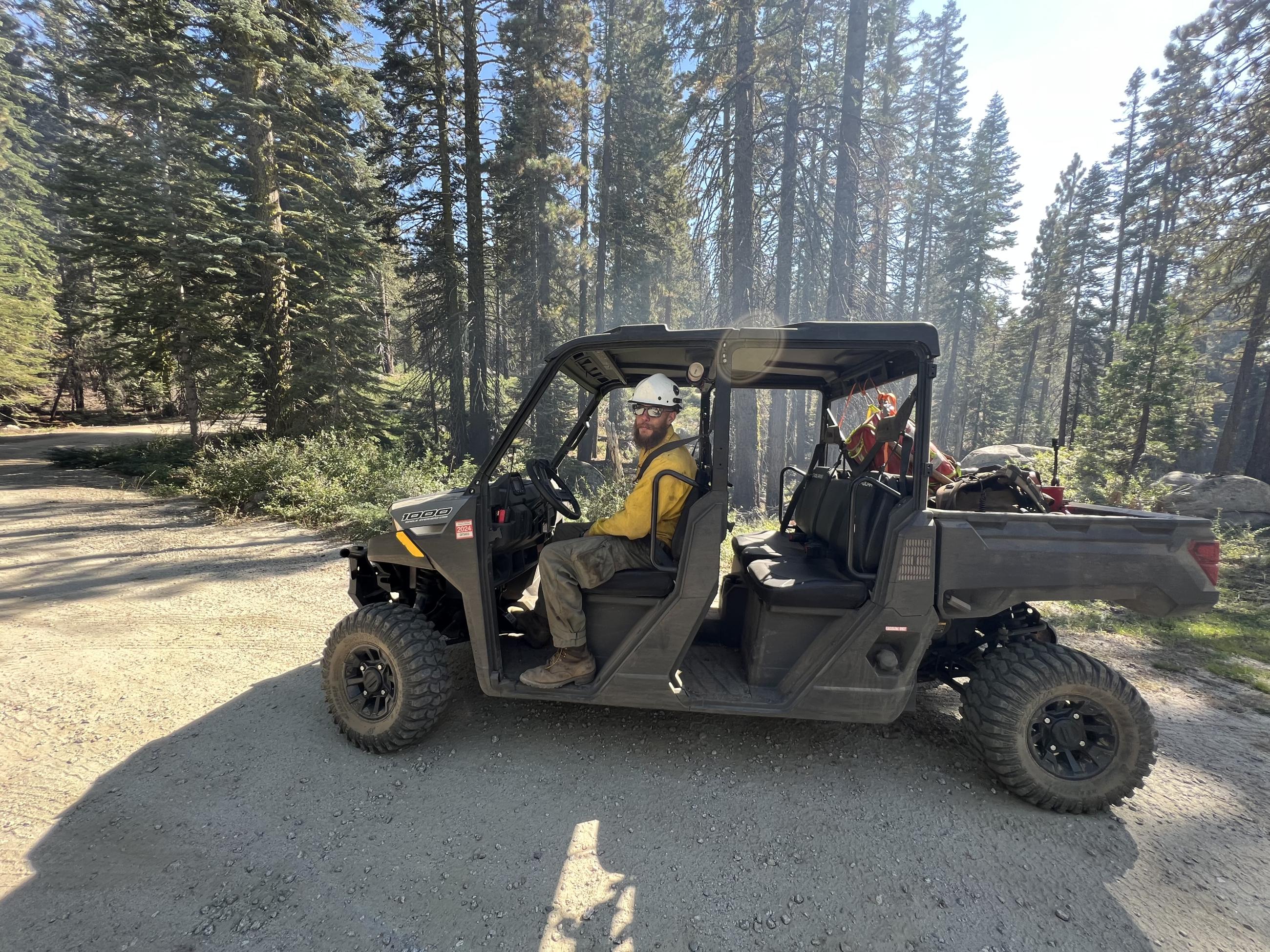 A wildland firefighter sitting in a quad surveys a forested landscape