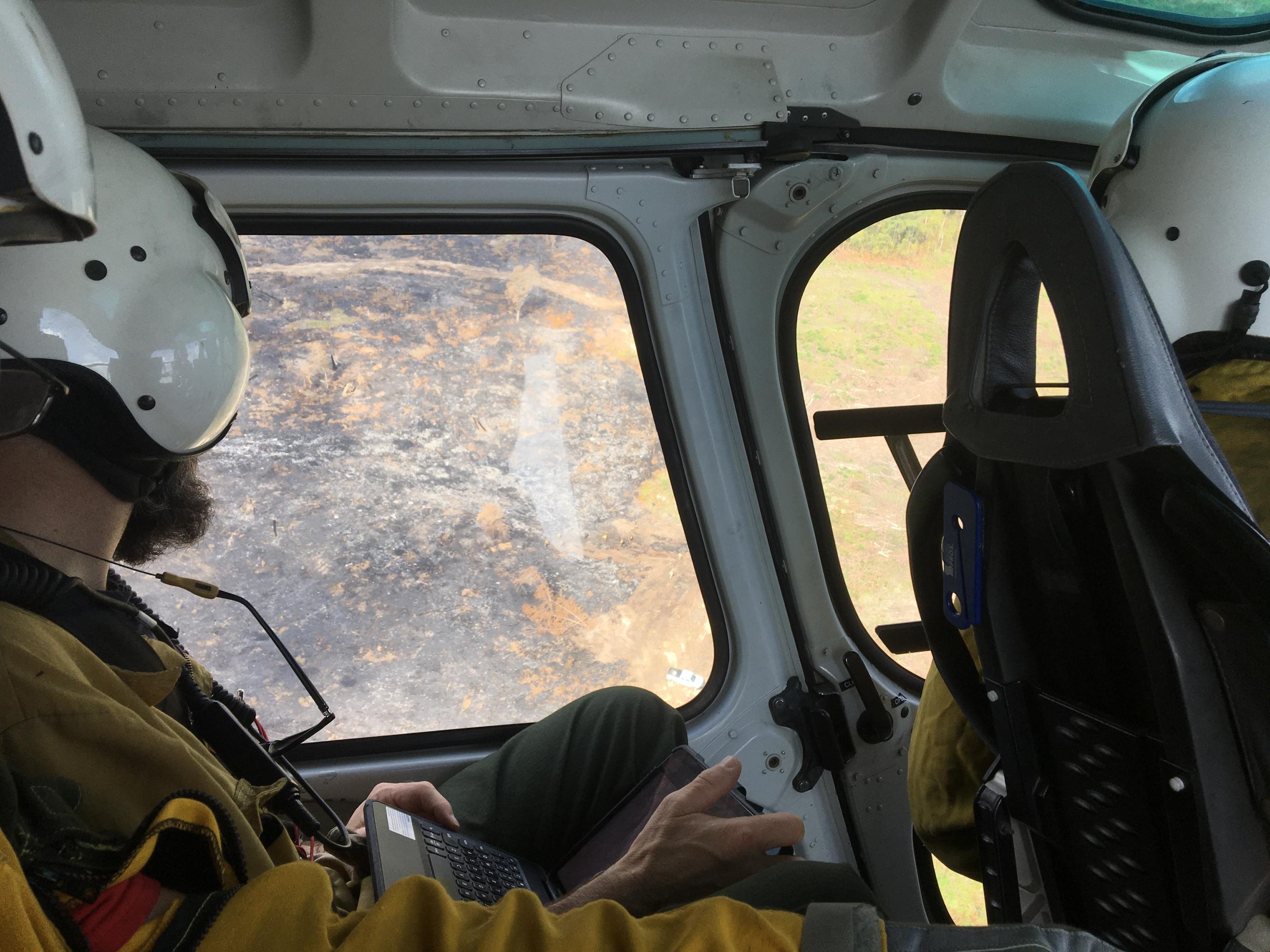 A firefighter in a helicopter looks out over burned area.