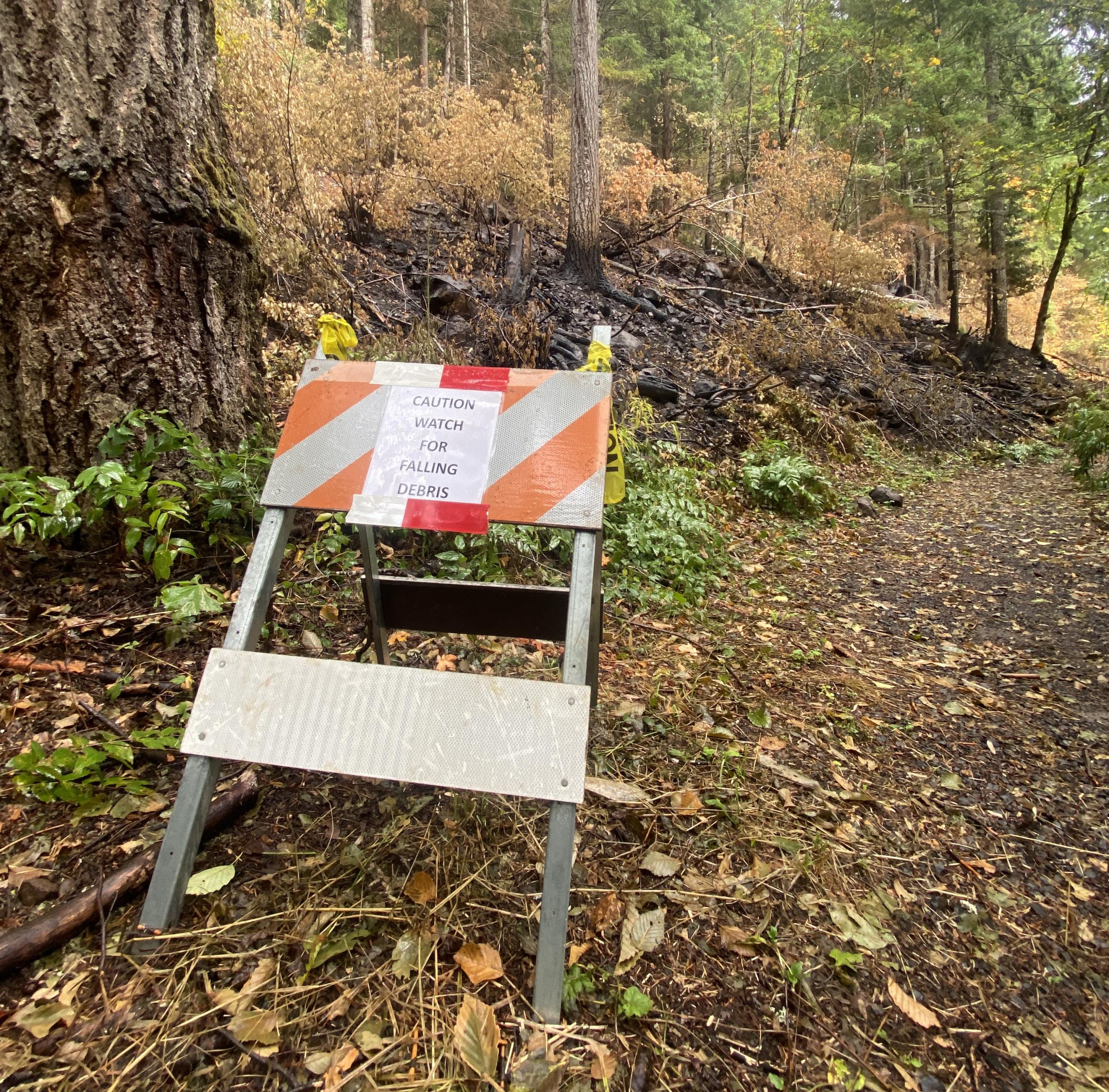 A caution sign is placed in front of a burned area with the words "Caution, watch for falling debris"