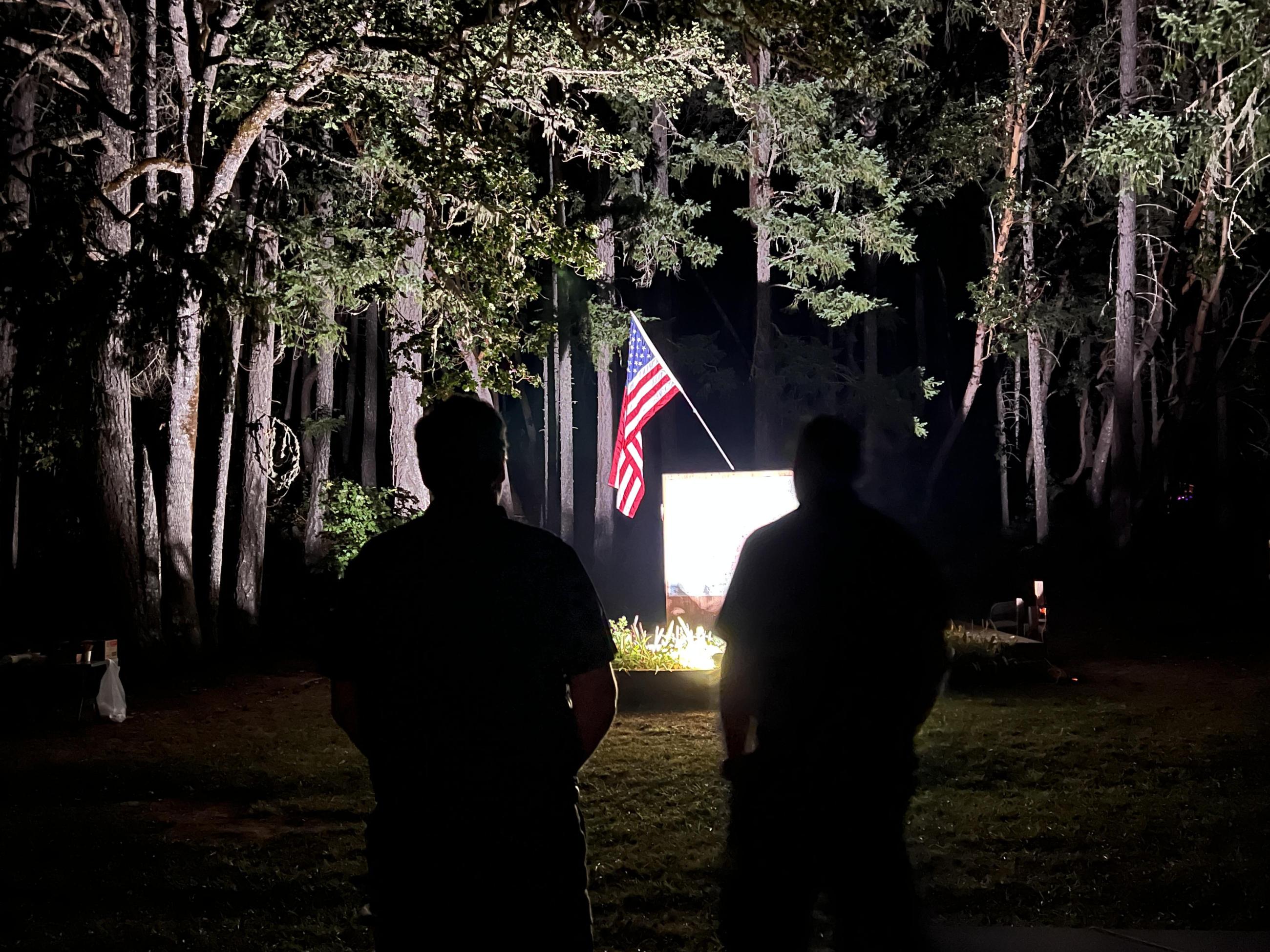 Two men silhouetted observing the flag lit up at night.