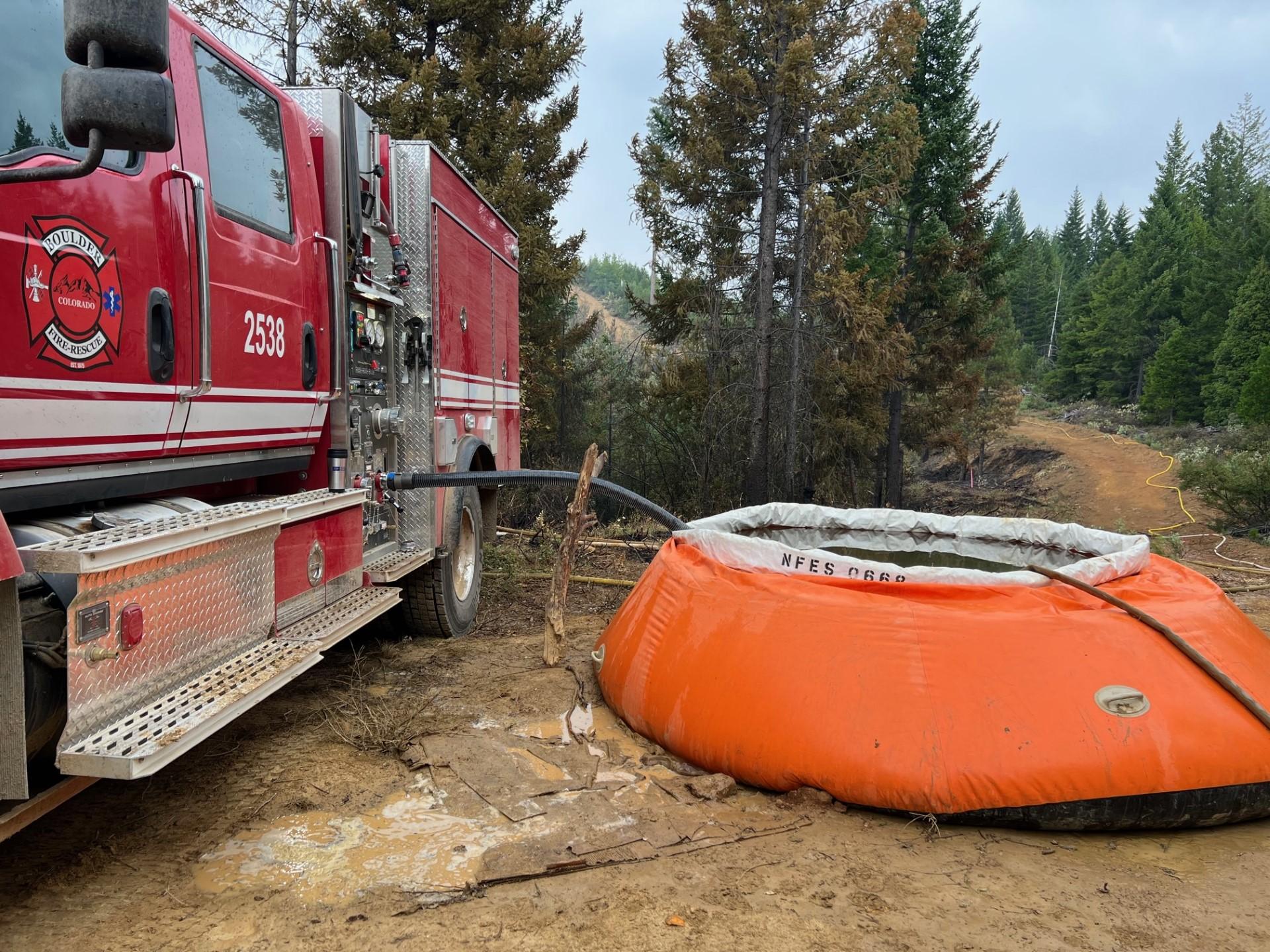 Image of a fire engine with an orange water tank on a dirt road next to a meadow in the forest. Photo USDA Forest Service courtesy Molly Cropp