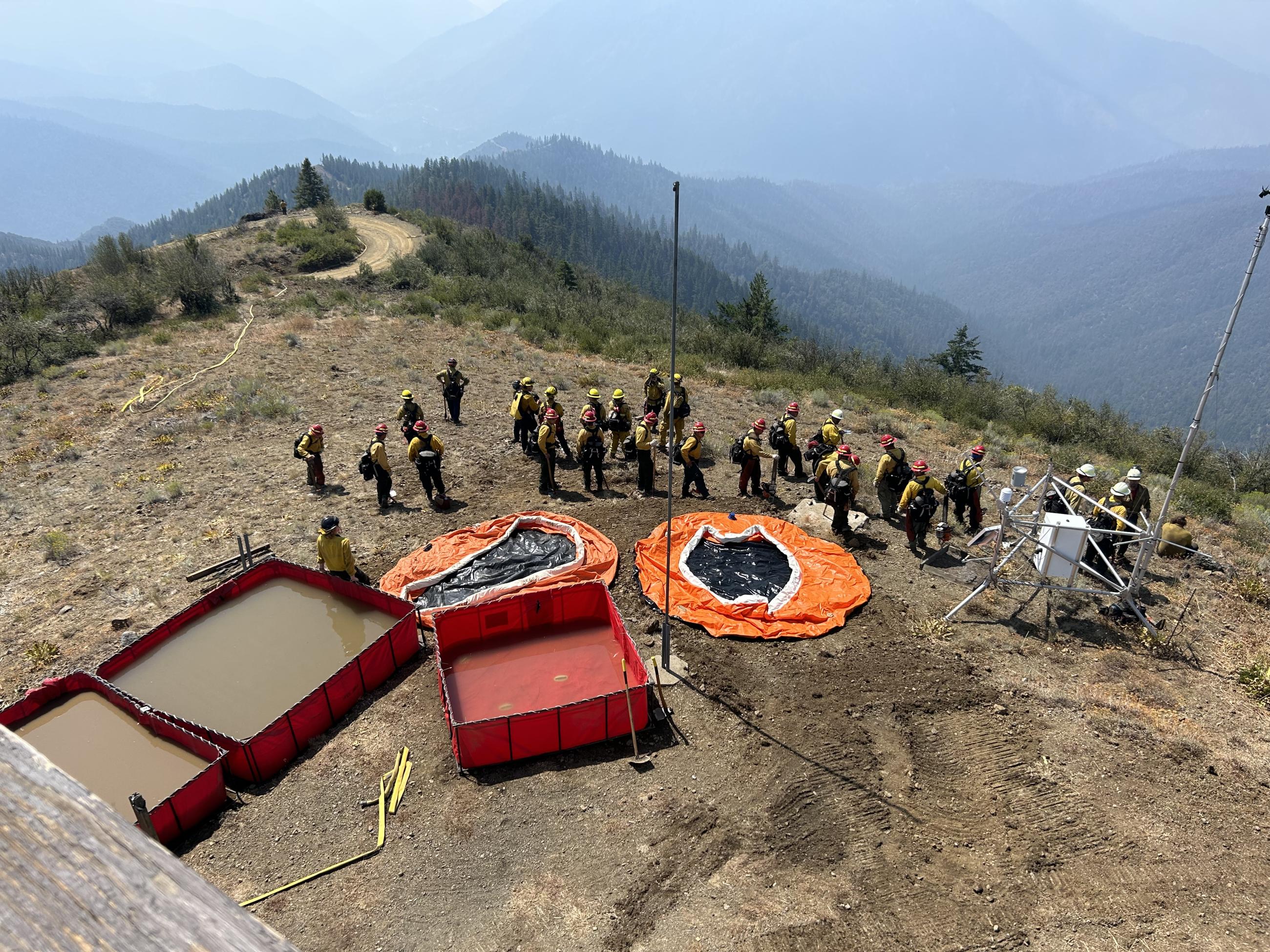 Image of water tanks being set up by firefighters on top of a mountain. Photo USDA Forest Service courtesy Allen Wehmuier