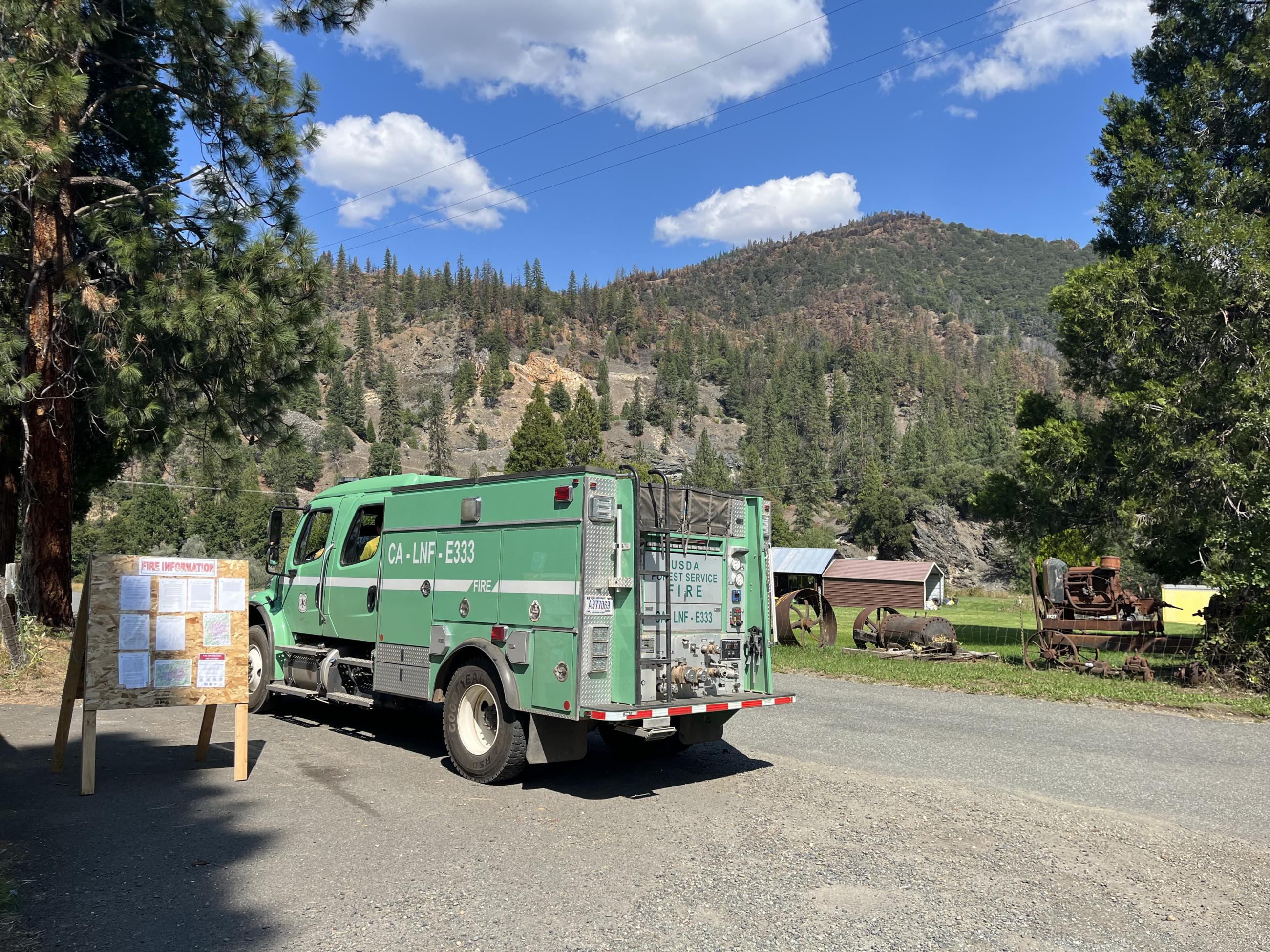 Image of a Lassen National Forest fire engine stopped by a fire information board with mountains around and clear skies. Photo USDA Forest Service courtesy Katie Julian