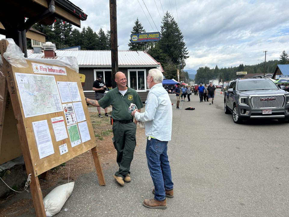 A Public Information Officer reviews information with the public in front of an information board.