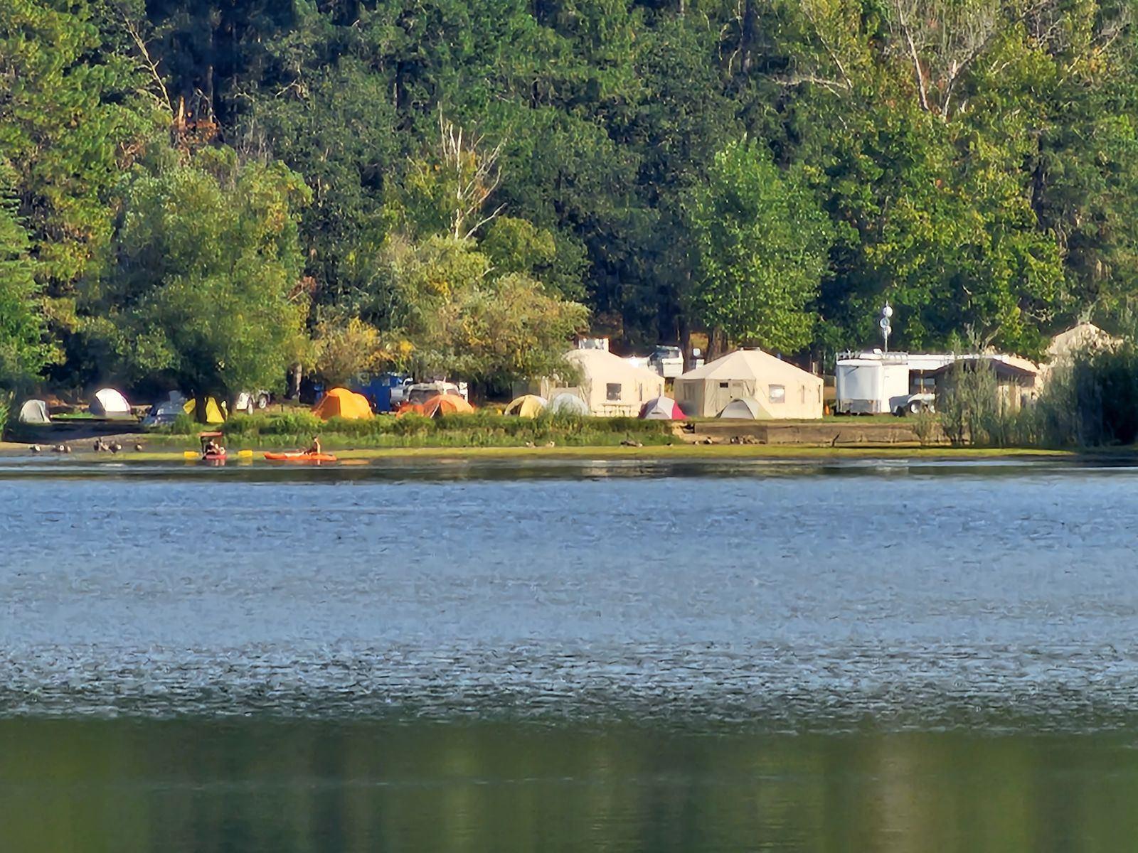 View across a lake of a collection of yurts making up the incident command post for the Smith River Complex.