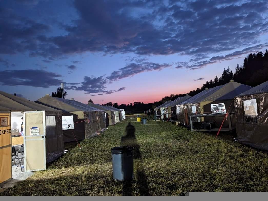 Yurts are setup at ICP in 2 rows with a purple and pink sunset in the background
