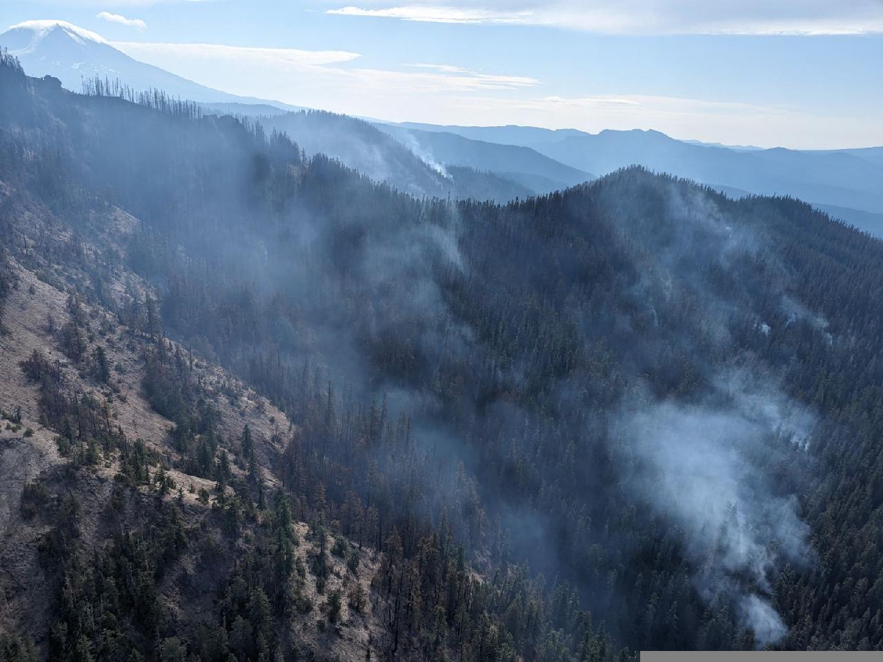 An view looking down over the rugged terrain with areas of smoke on the Snagtooth fire