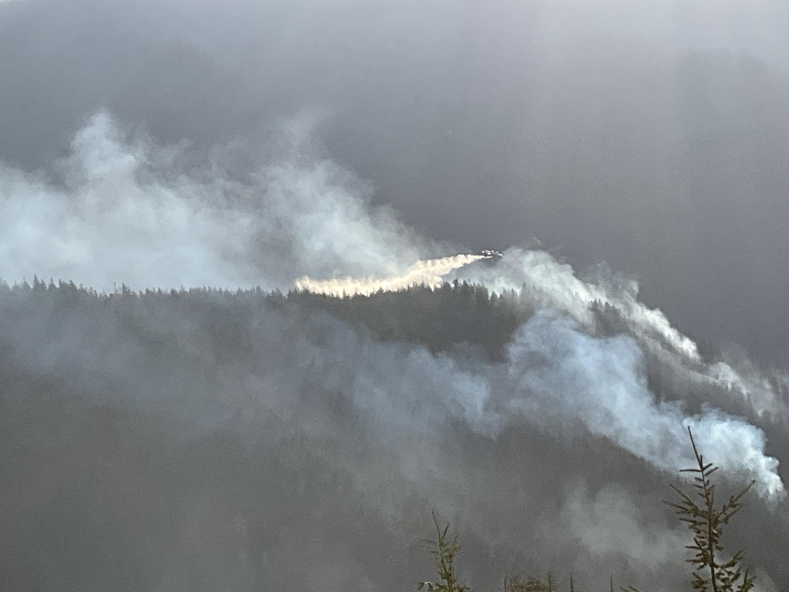 Airplane drops water onto a smoky, forested ridgetop