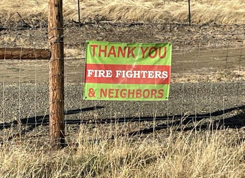 A green and red banner reading "Thank you Firefighters and Neighbors" hangs on a fence