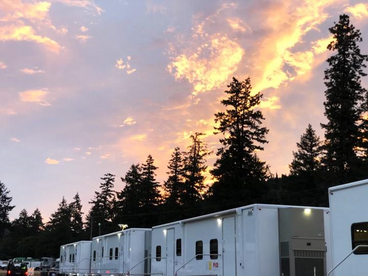 Pink and yellow morning sky above a row of trailers, with tall conifers behind them