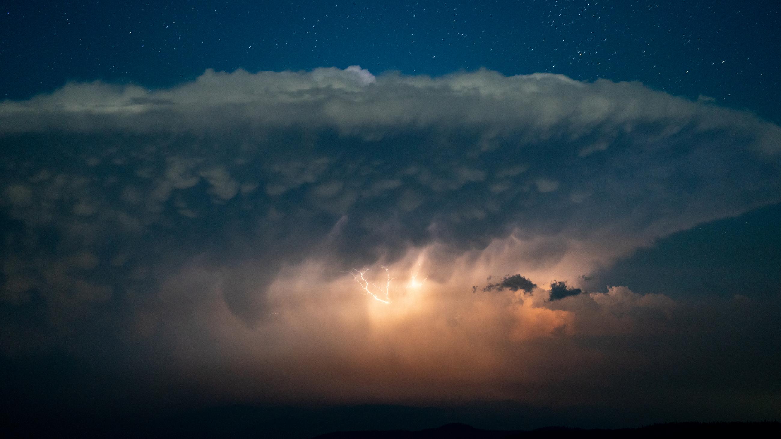 Bright lightning crashes from a large cloud into the night sky