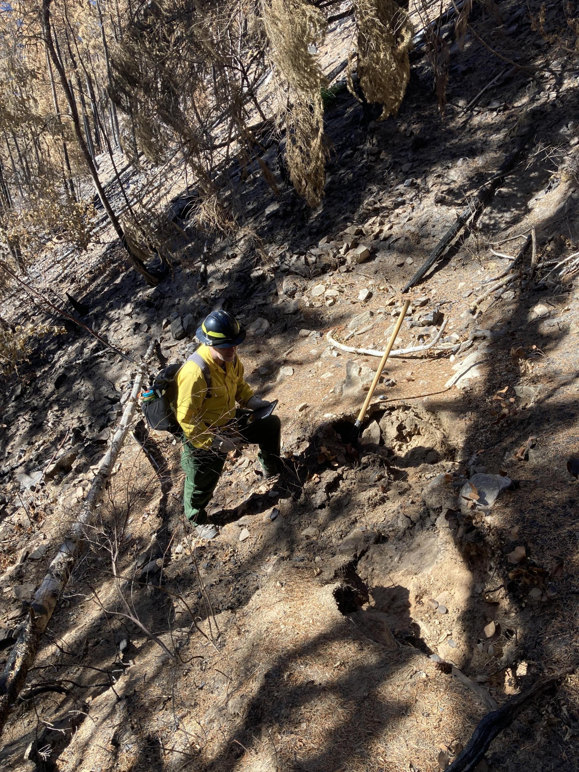 A man in a helmet and yellow shirt stands on a dirt trail surrounded by dirt