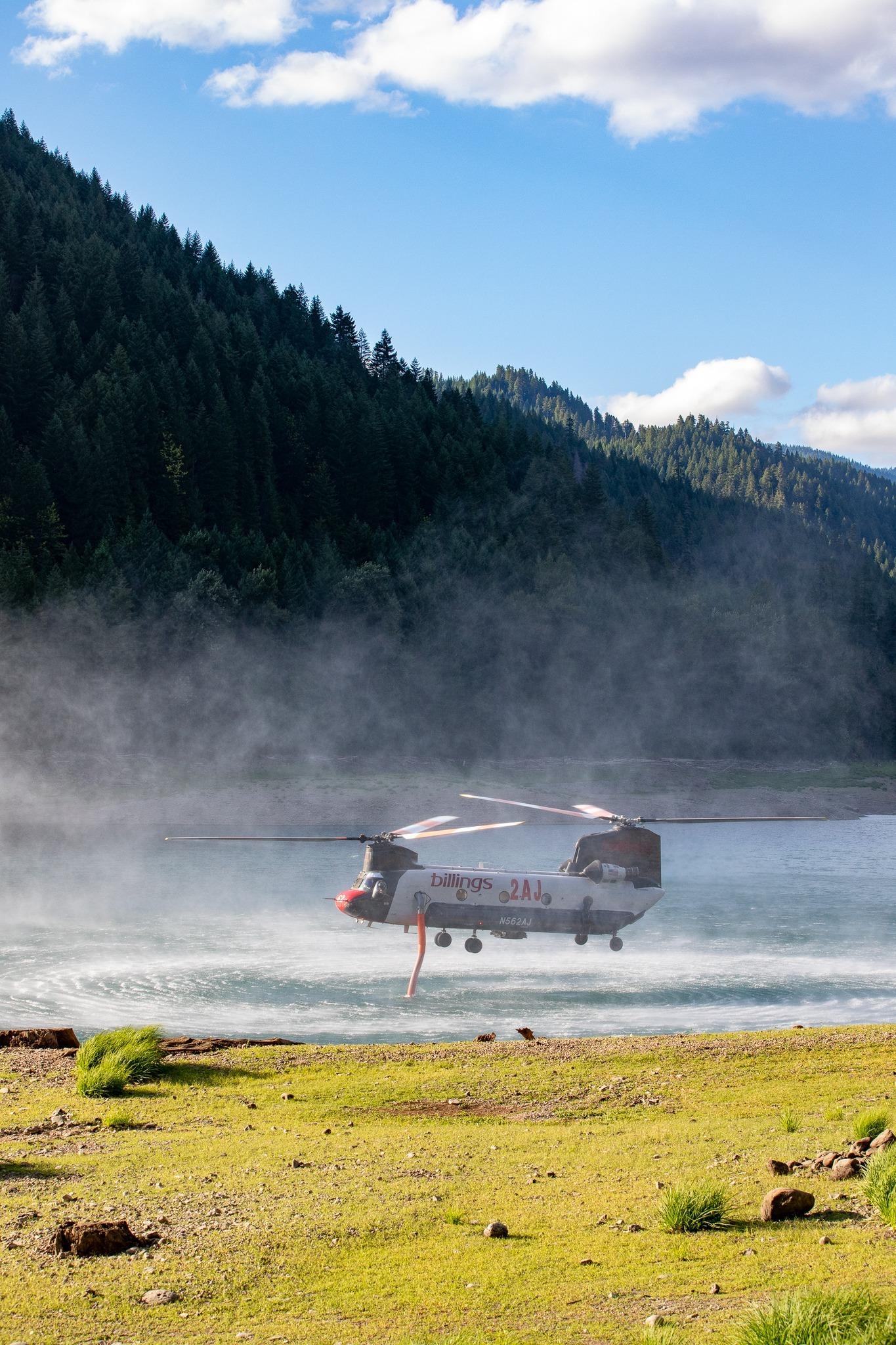A helicopter hovers over a Lake while it fills with water.