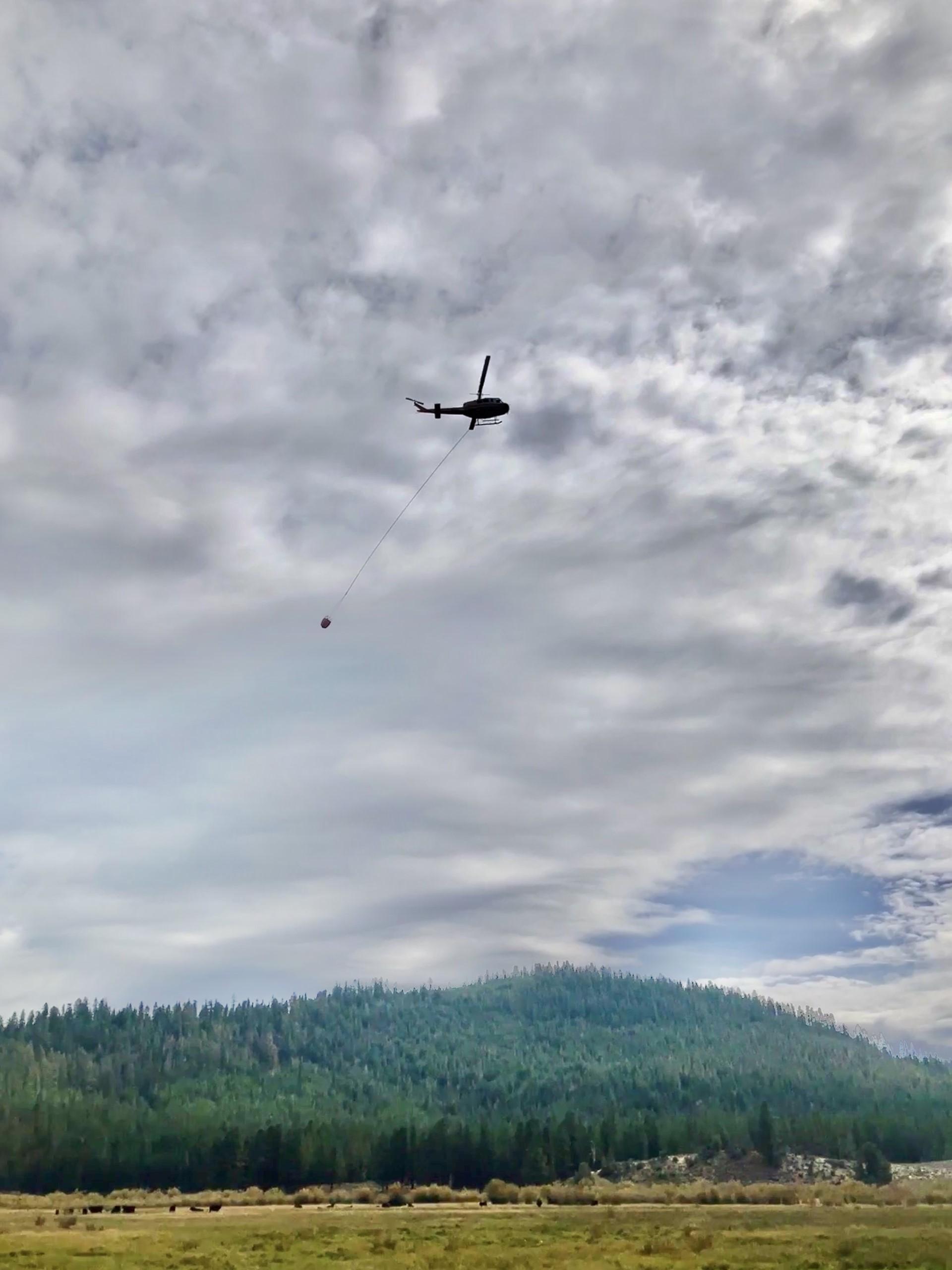 A picture of a helicopter with a water bucket working over the fire today. 