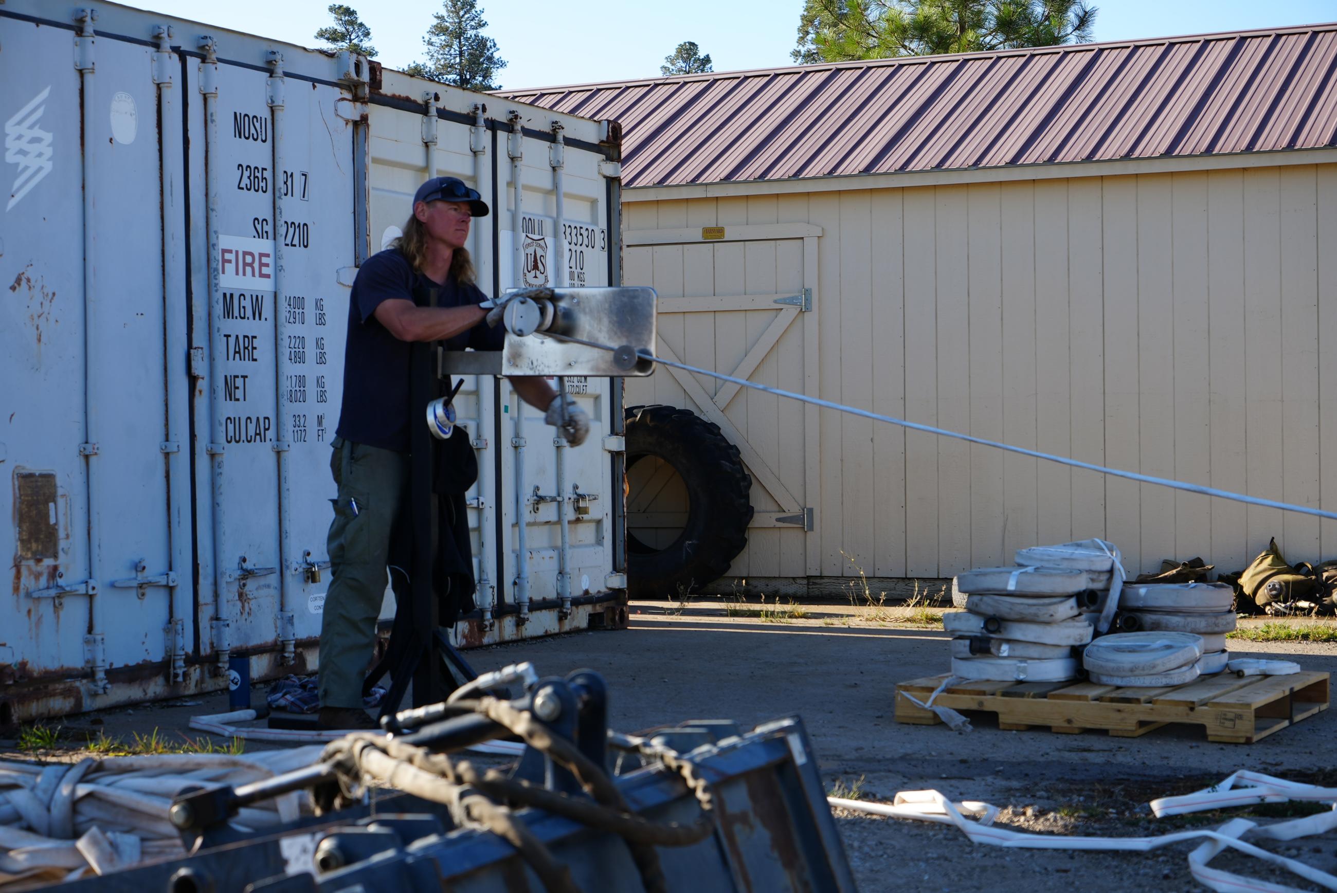 Firefighter Tyler Kuhn uses a device to roll up firehose no longer needed on the Bear Creek Fire