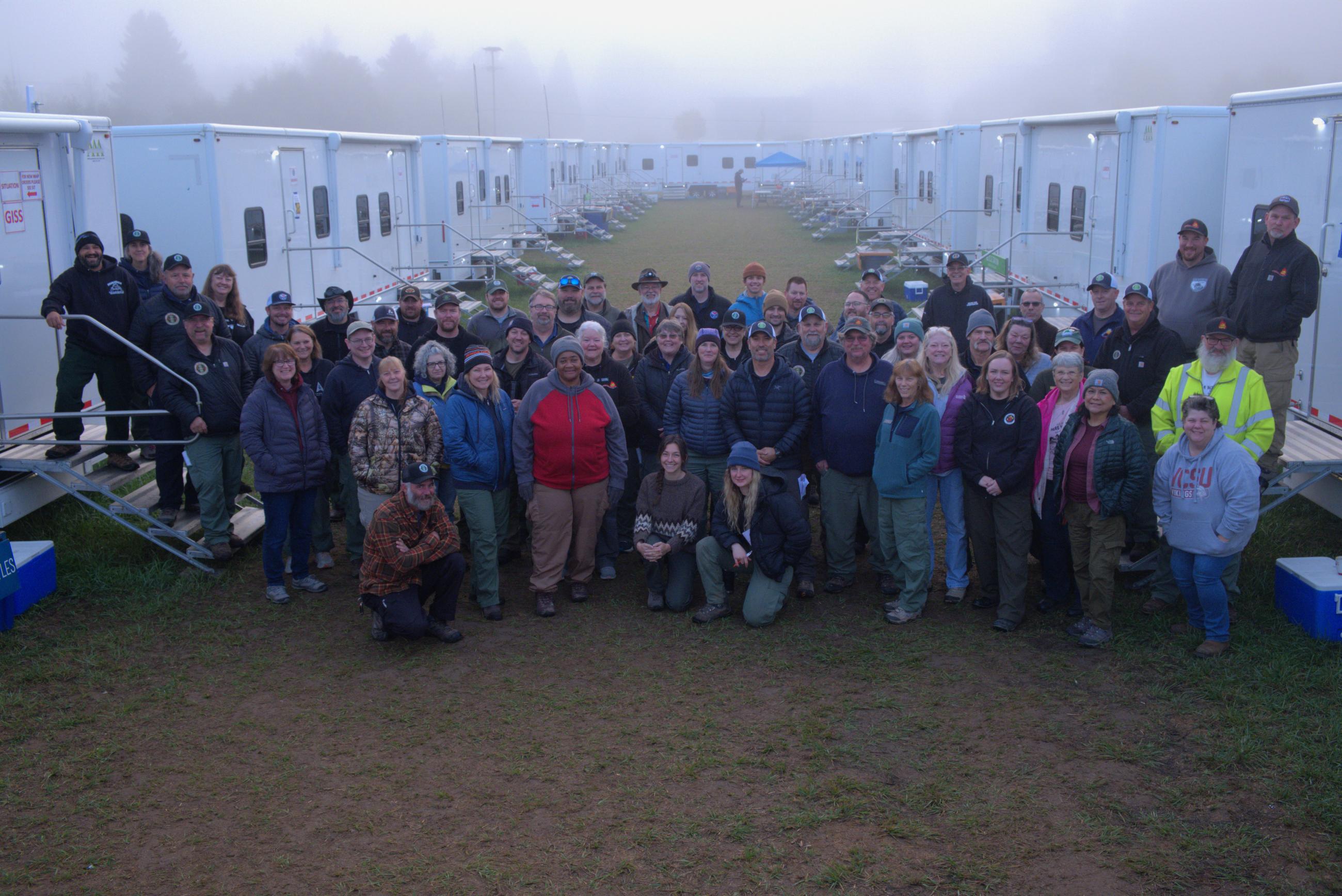 Approximately 50 members of Northwest Incident Management Team 10 pause for a photo on the grass between the trailers that serve as offices while the team manages the Lookout, Bedrock, Petes Lake, Horse Creek and Pothole Fires