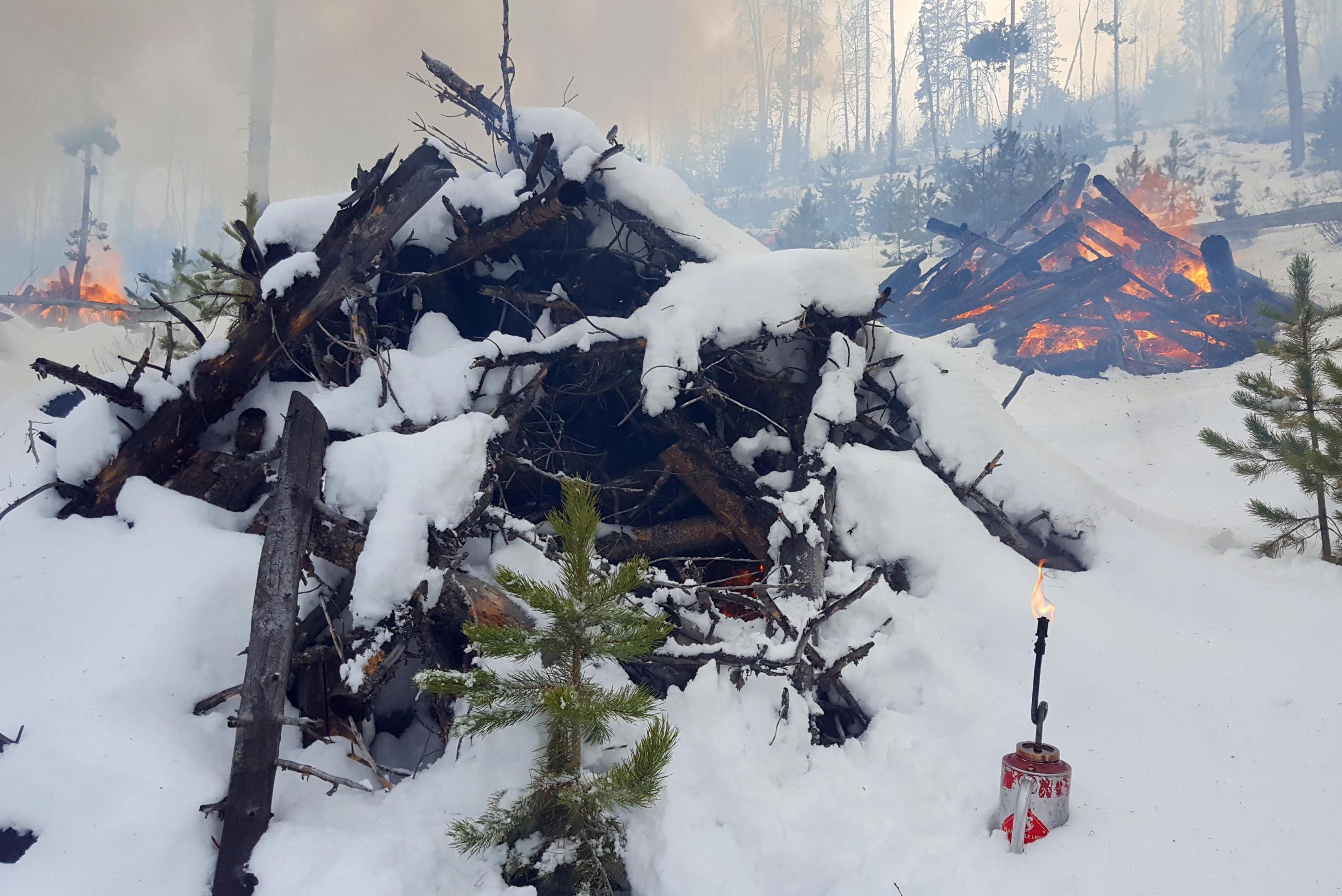 Pile burning in snow with smoke, flames