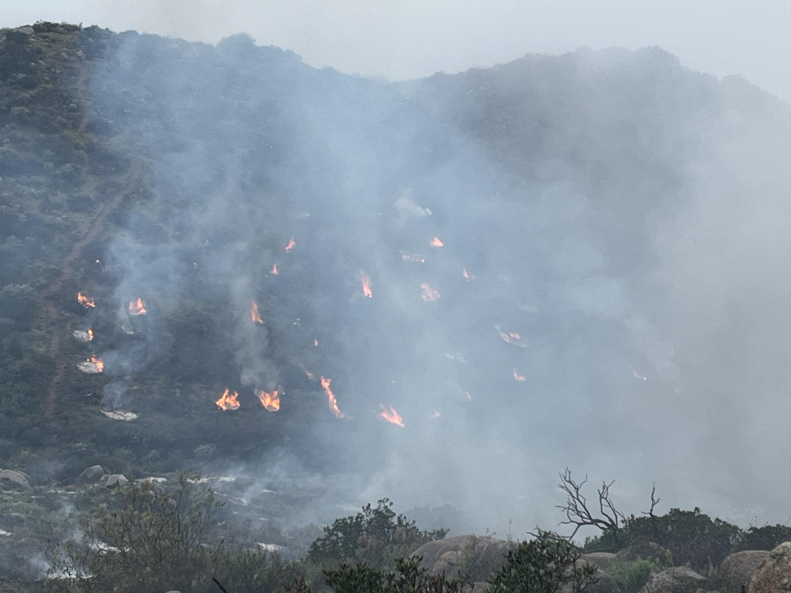 Image of mountains in the background with a lot of smoke and fuels on fire.