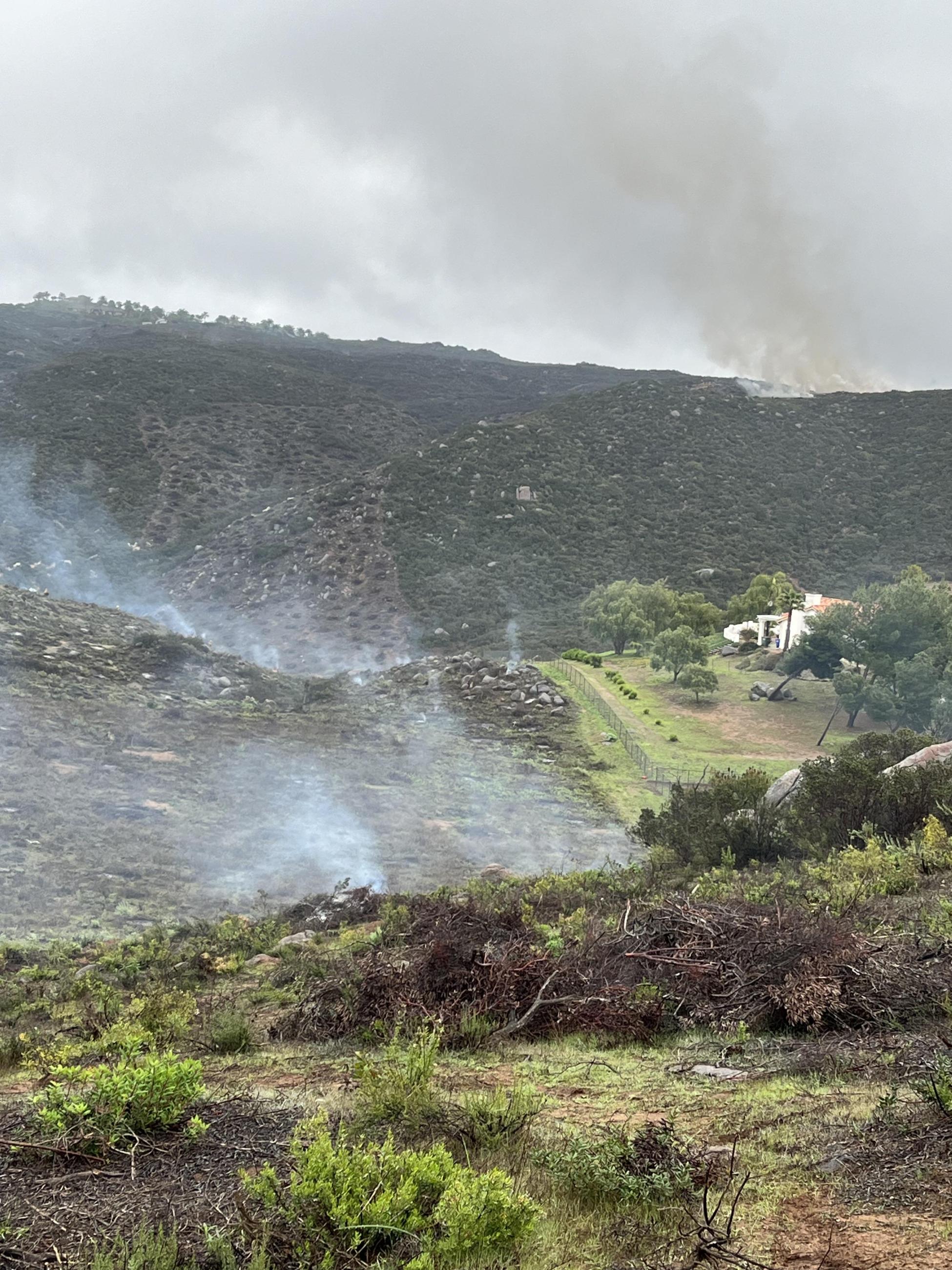 Image of mountains in the background a building and smoke from the Ramona Fuel Break Project.