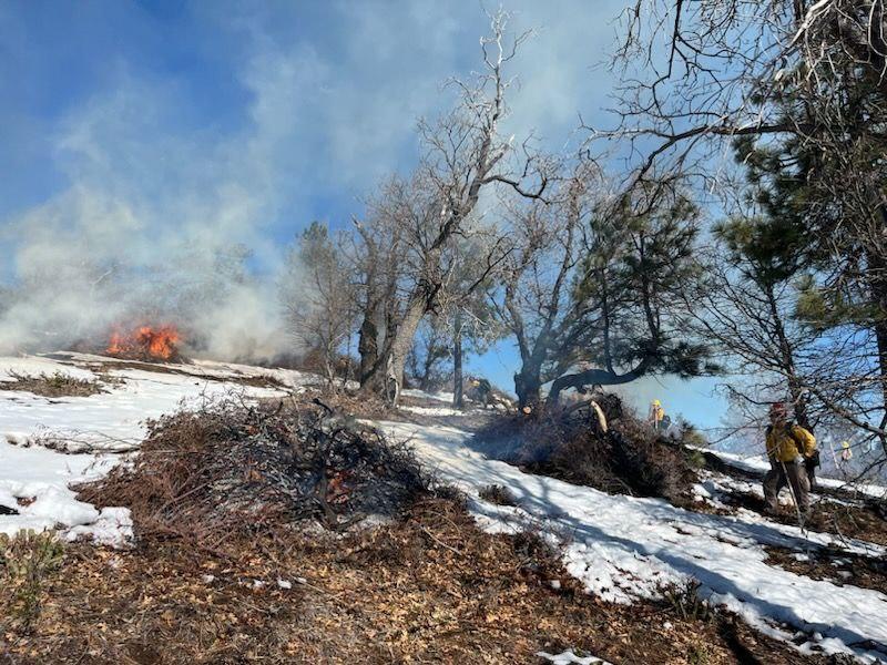 Image of snow ont he ground with fire, smoke, and firefighters working on the Mount Laguna Prescribed burn.