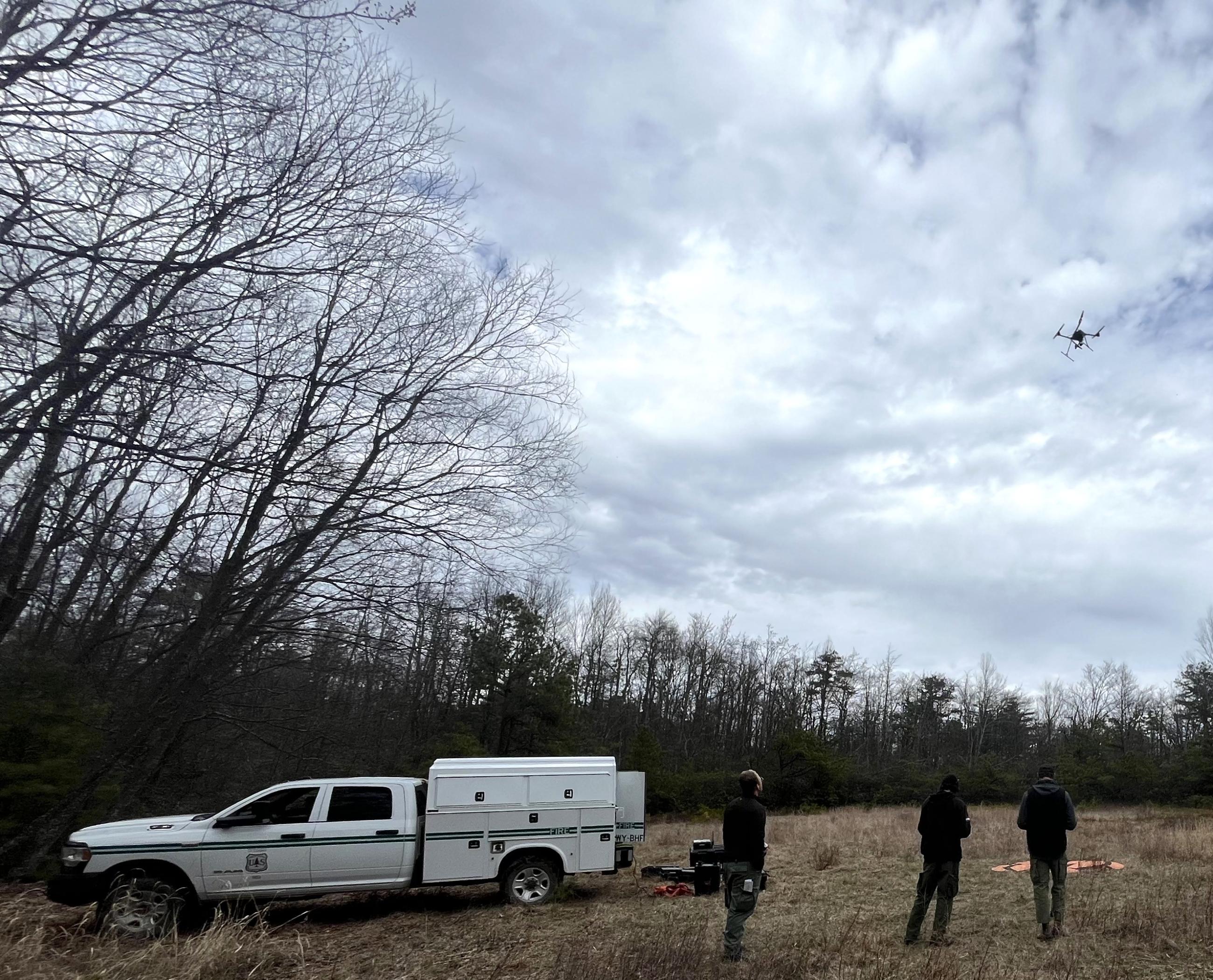 Three firefighters standing next to a US Forest Service truck in a field with a drone overhead