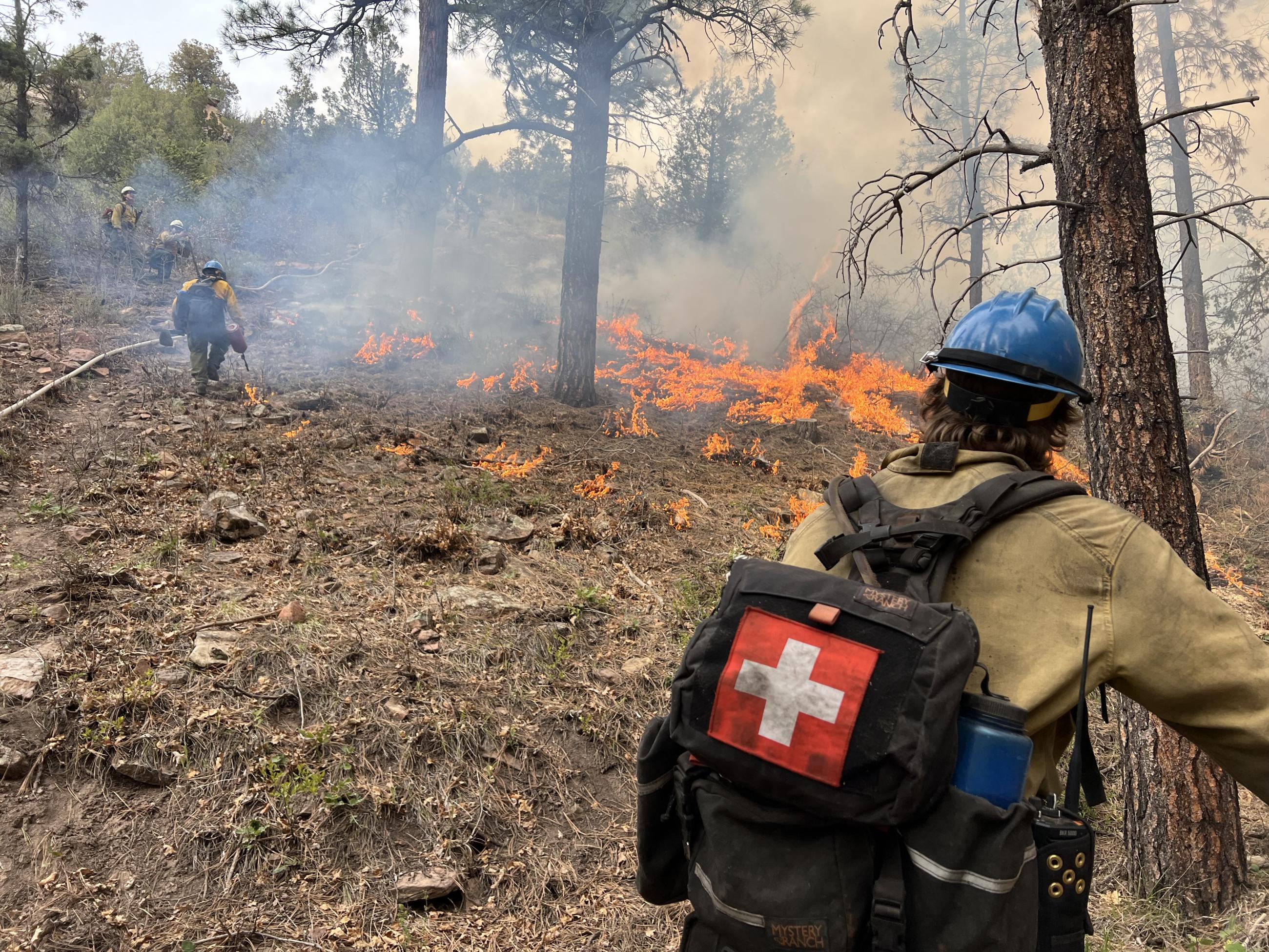 A firefighter with a medical cross on his pack is seen near a prescribed fire on the San Juan National Forest.