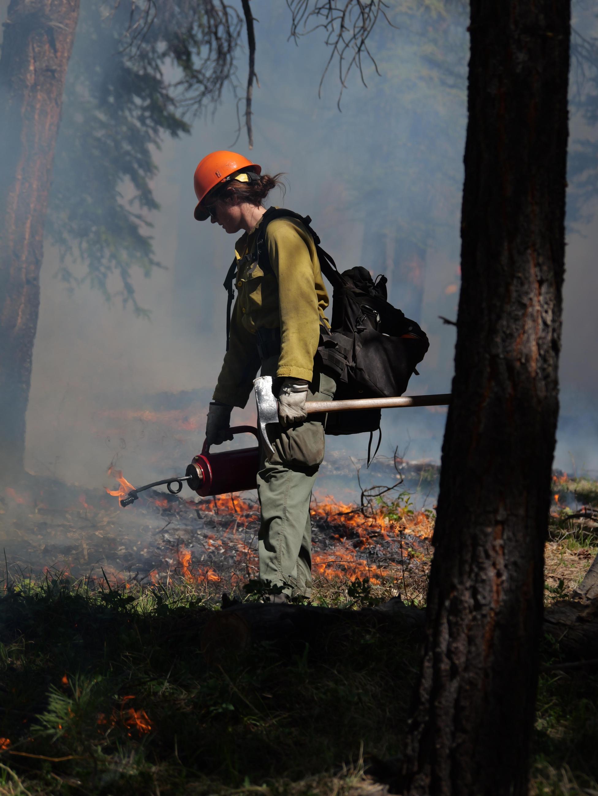 A female firefighter is seen with an axe and drip torch during the Spruce Creek Fire.