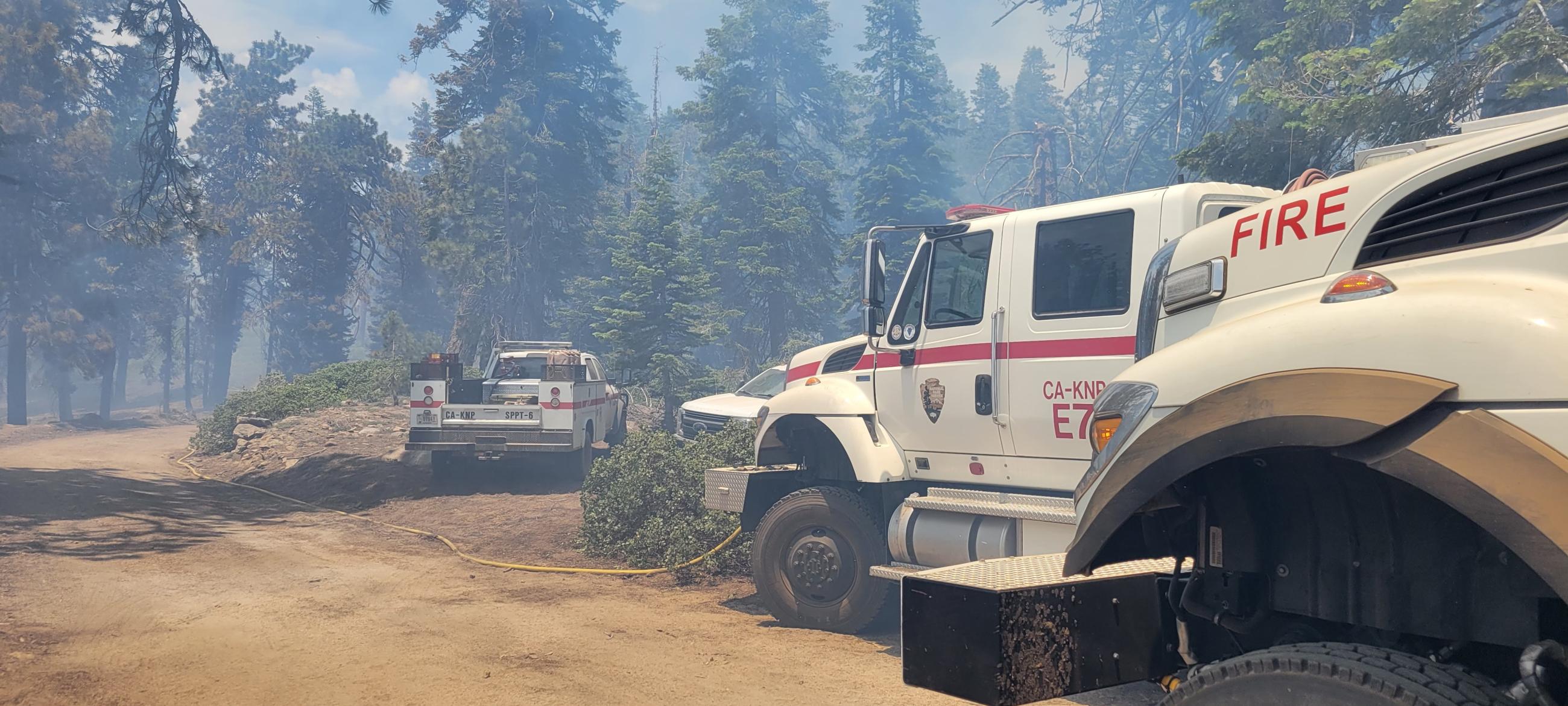 Picture of National Park Service fire trucks with forest and smoke in the background.