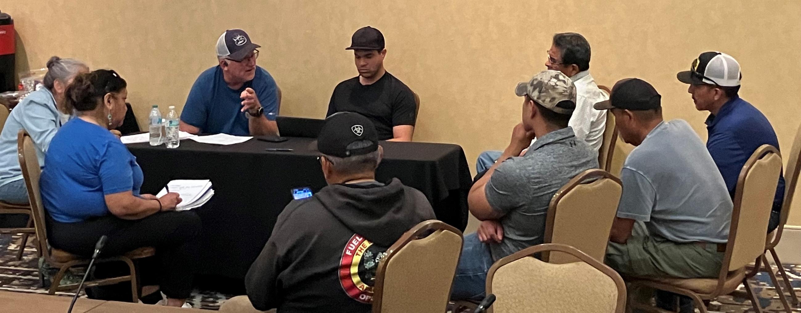 Burned Area Emergency Response (BAER) forestry specialist Eric Rhodenbaugh and Chris LaCroix meet with Mescalero Apache Tribe leadership and natural resources staff inside. People in meeting seated in circle in conversation..