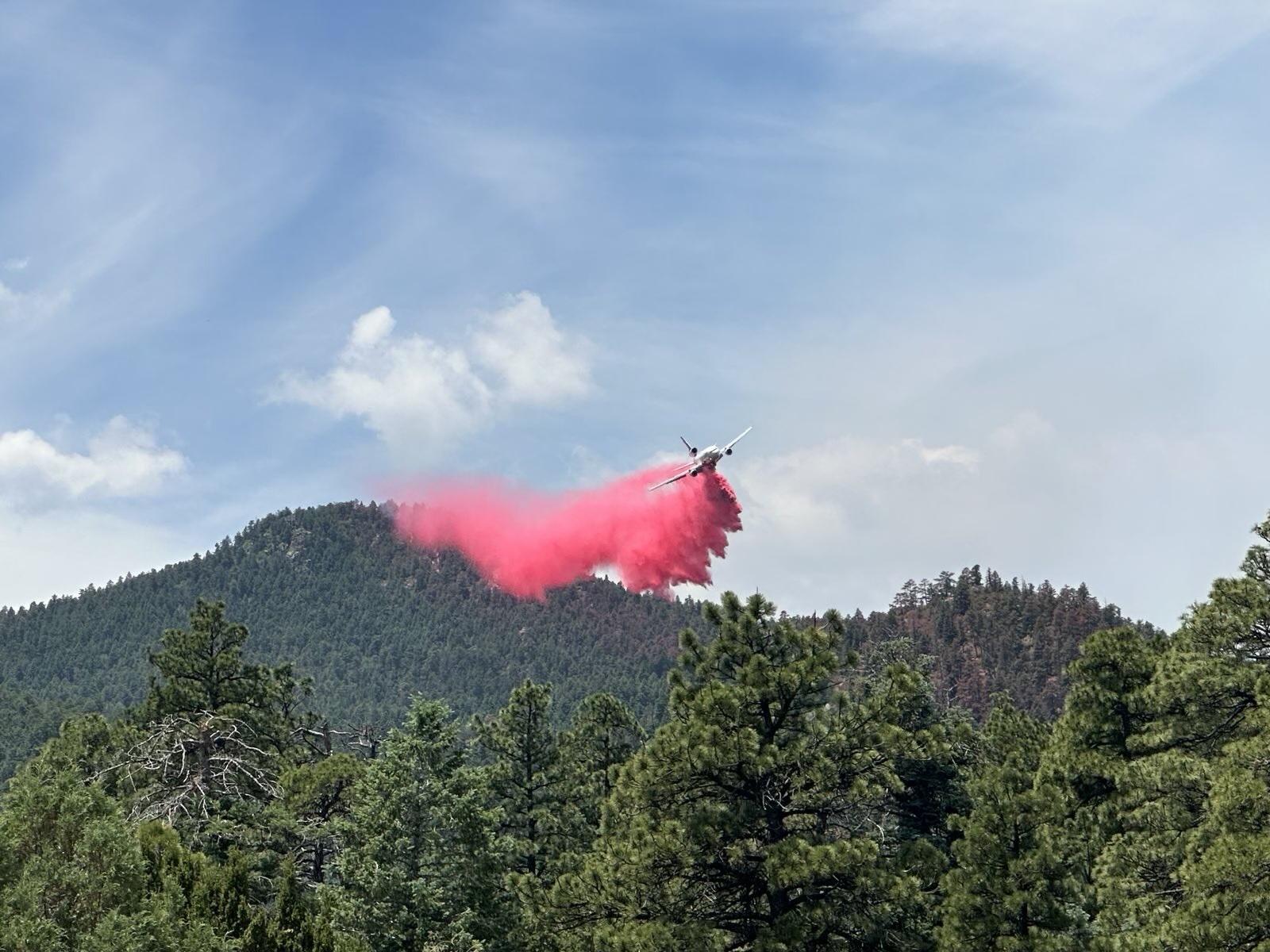 An air tanker drops a load of red fire retardant above evergreen filled mountain backdrop. 