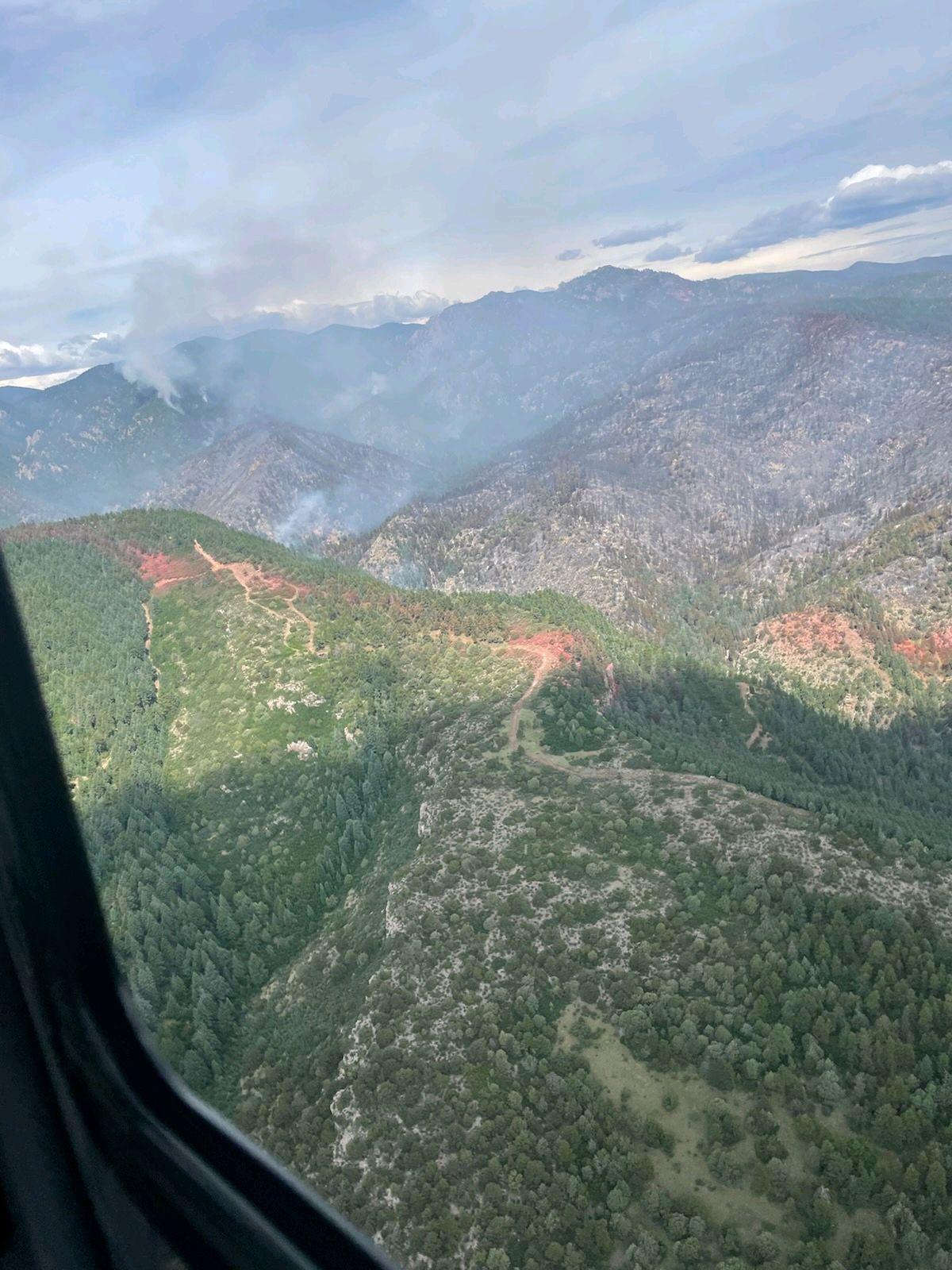 An aerial view of red fire retardant lines that have been laid on the ground. The landscape is rolling with evergreen trees. 