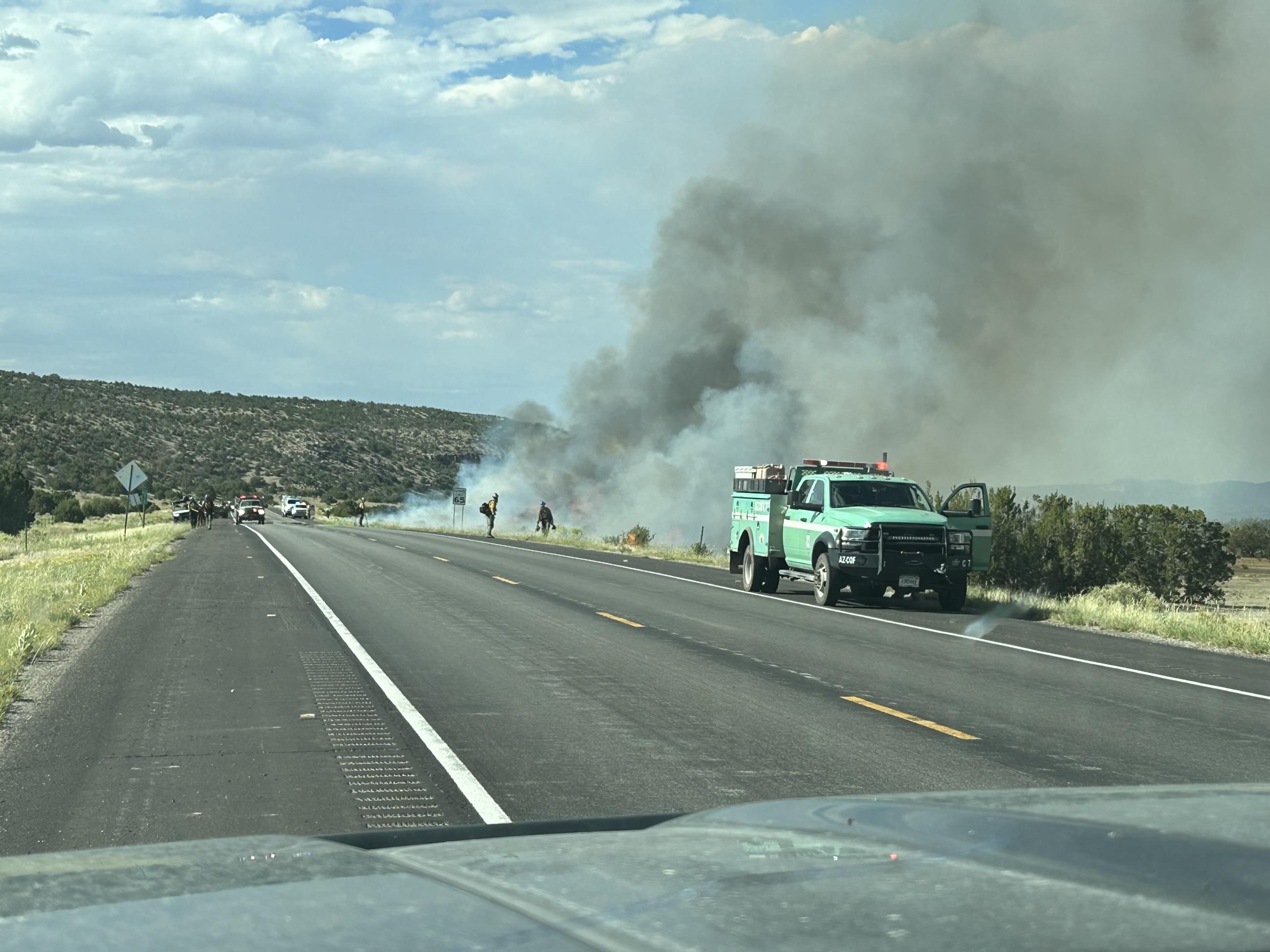 Firefighters work along the roadway of Highway 53 during the Encerrita Fire as a smoke plume rises behind them and their vehicles