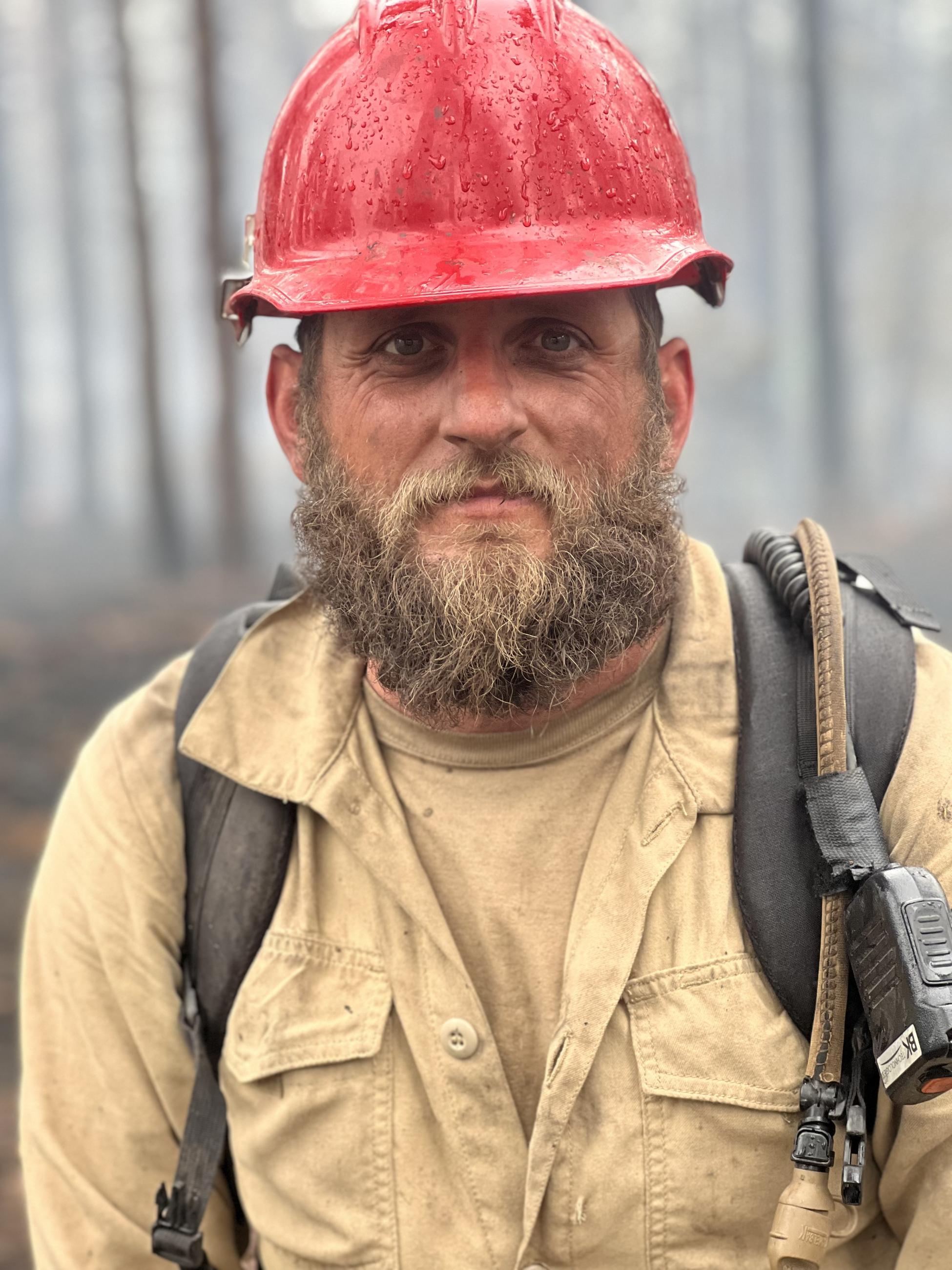 A firefighter in a red helmet and wearing a pack is shown.