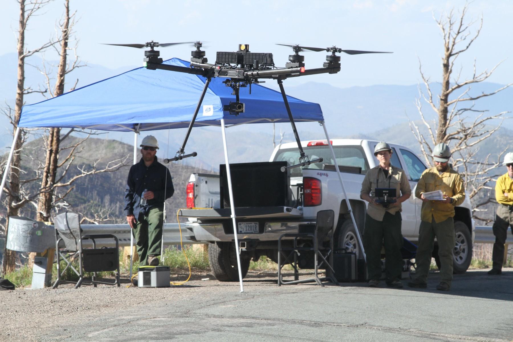 Drone lifting off the ground with firefighters controlling it in the background