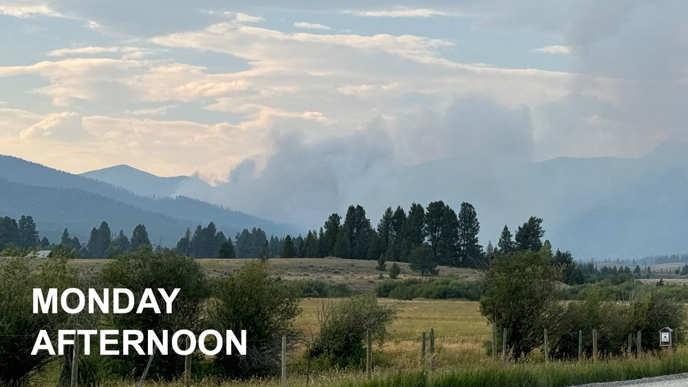 Long shot of dark smoke over forested mountains in the distance