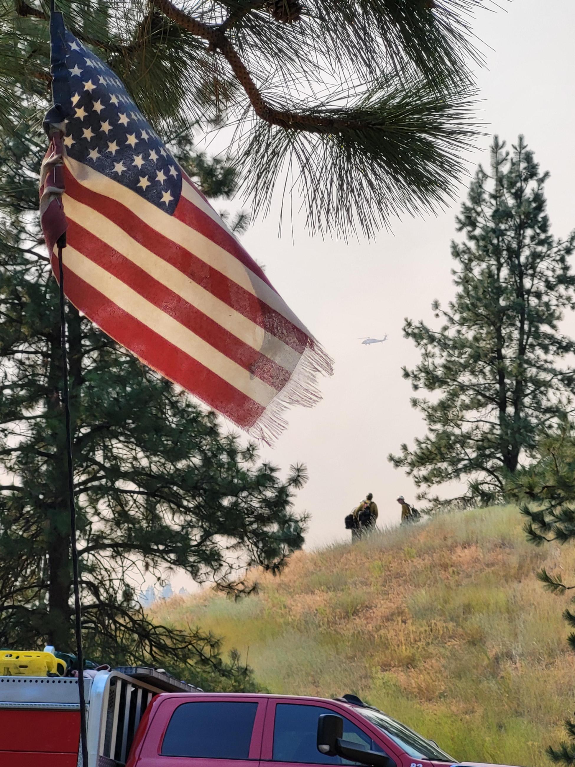 The American Flag in the foreground with firefighters on a hill in the far ground