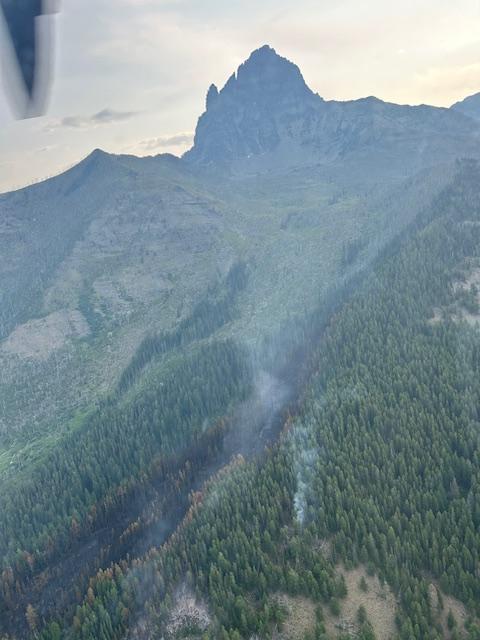 Burn scar with multiple small smoke plumes in front of mountain peak