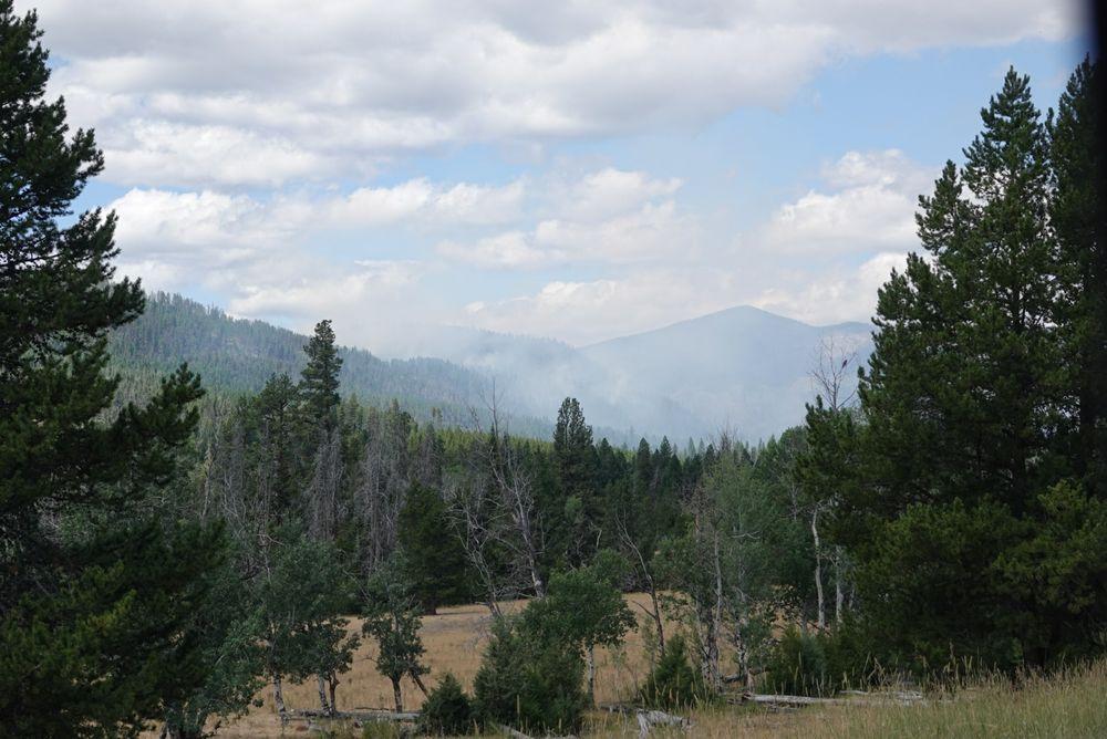 Trees on left and right foreground. Smoke partially obscuring mountain in center back.