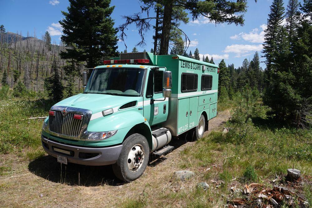 Forest Service green transport vehicle parked on dirt pad in front of trees