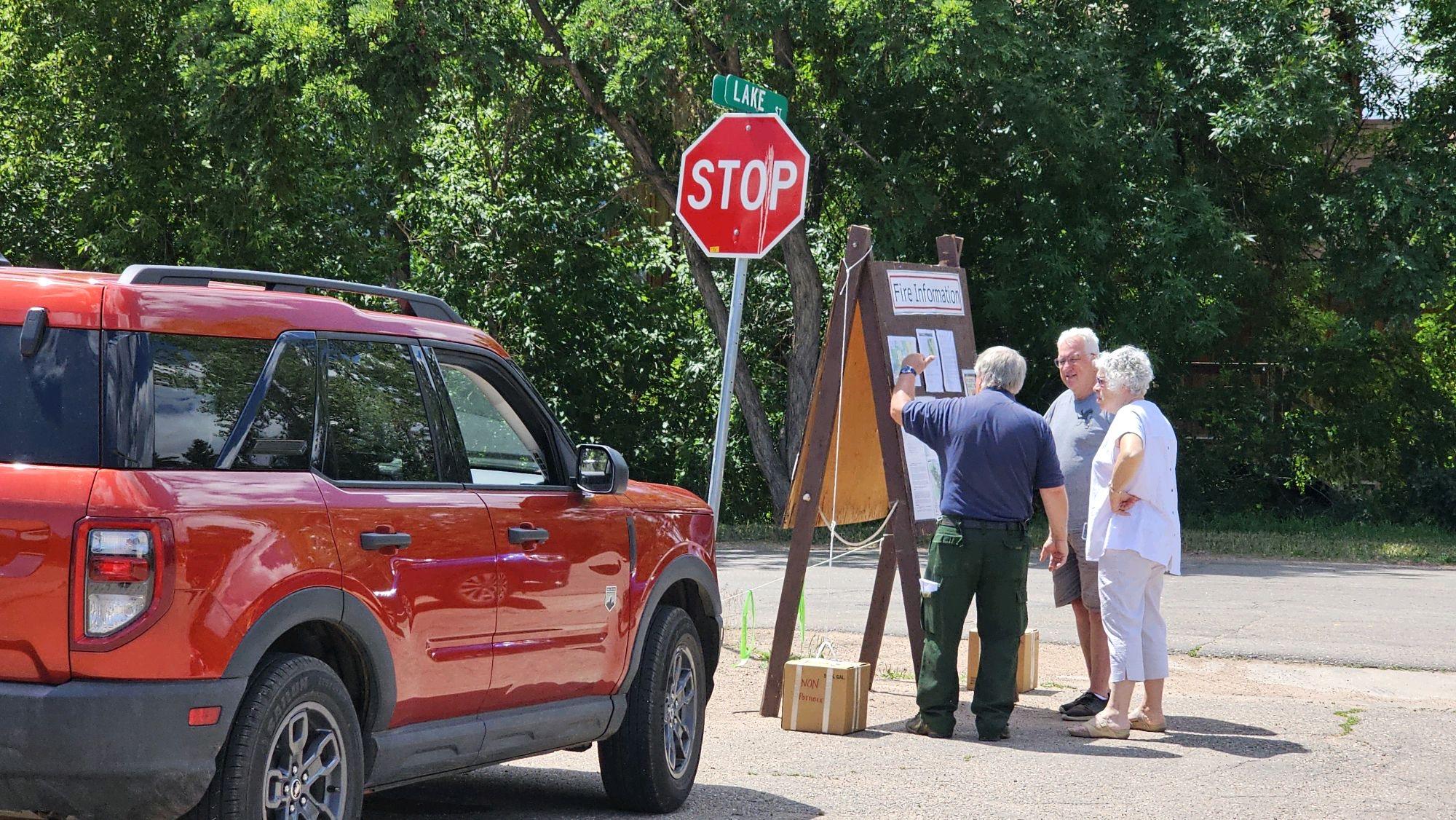 A public information officer is talking to two members of the public. They are standing at an information bulletin board.