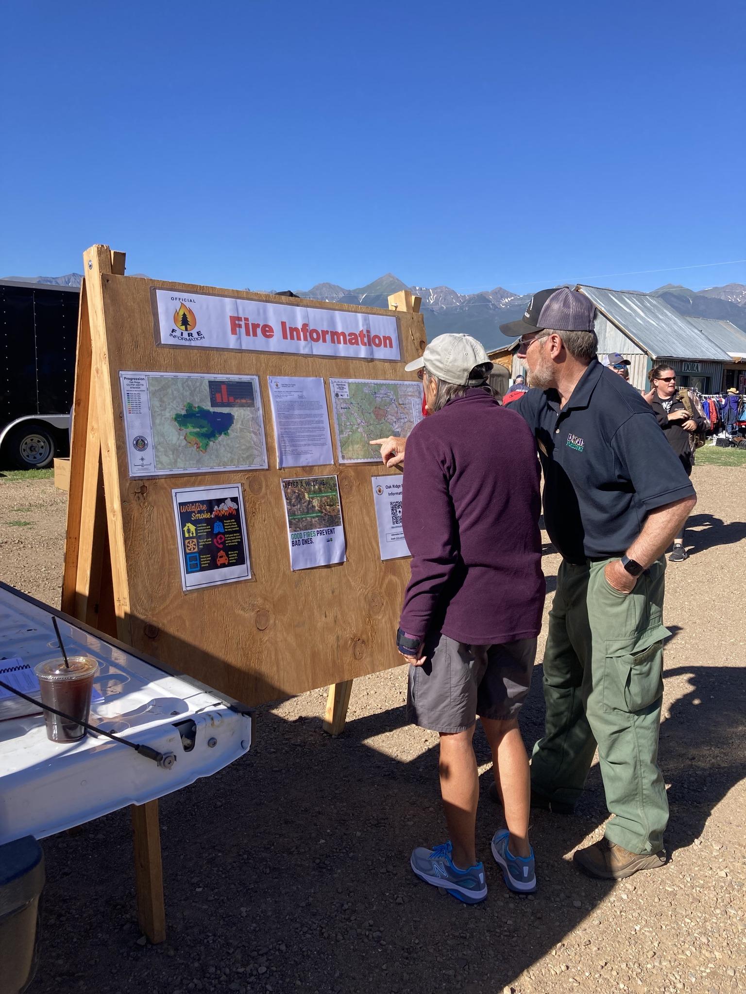 A public information officer for the fire talks with a member of the public. They are looking at information that has been posted on a public information board.