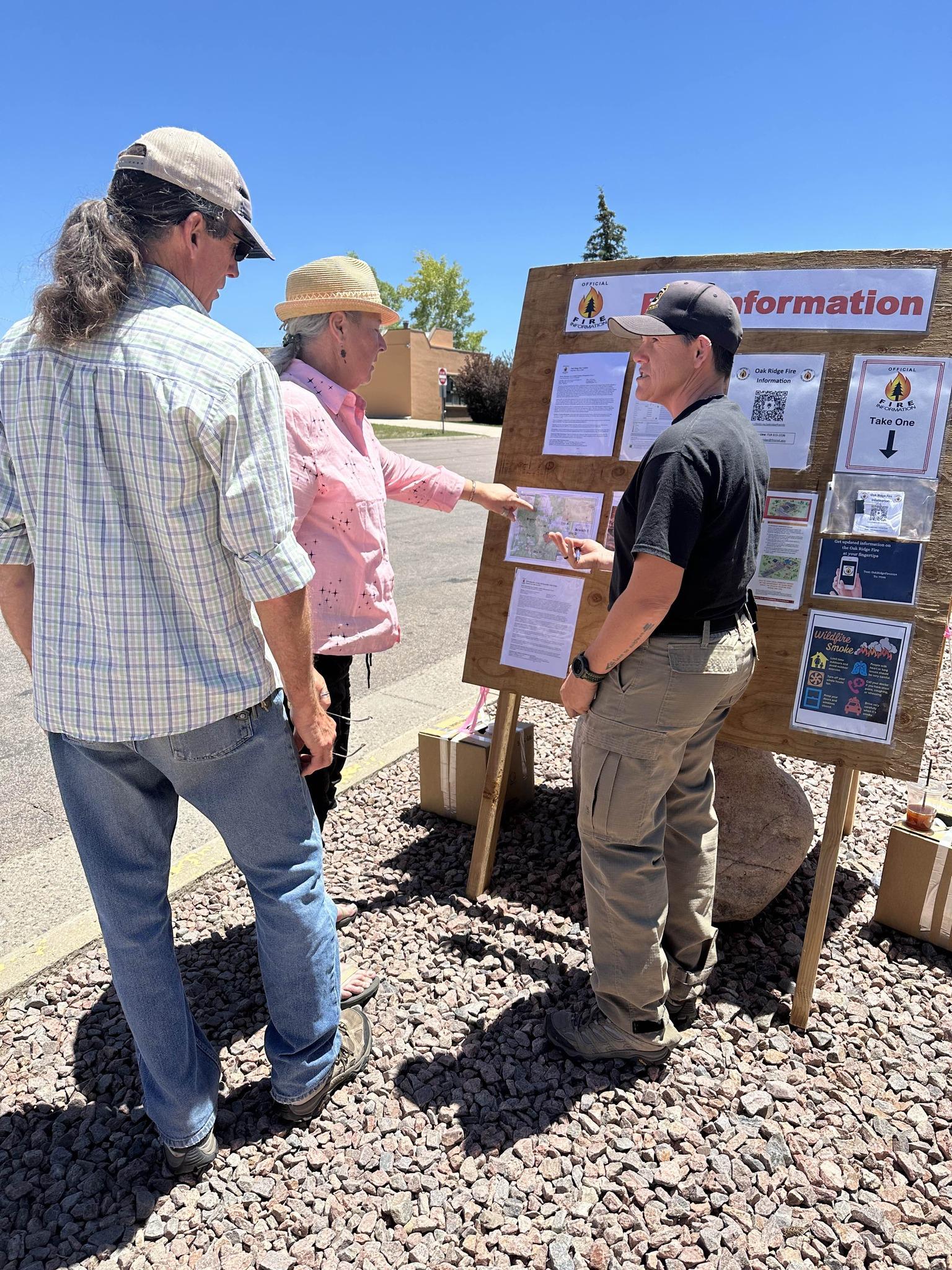 Two members of the public are talking to a public information officer that is staffing a public information board.