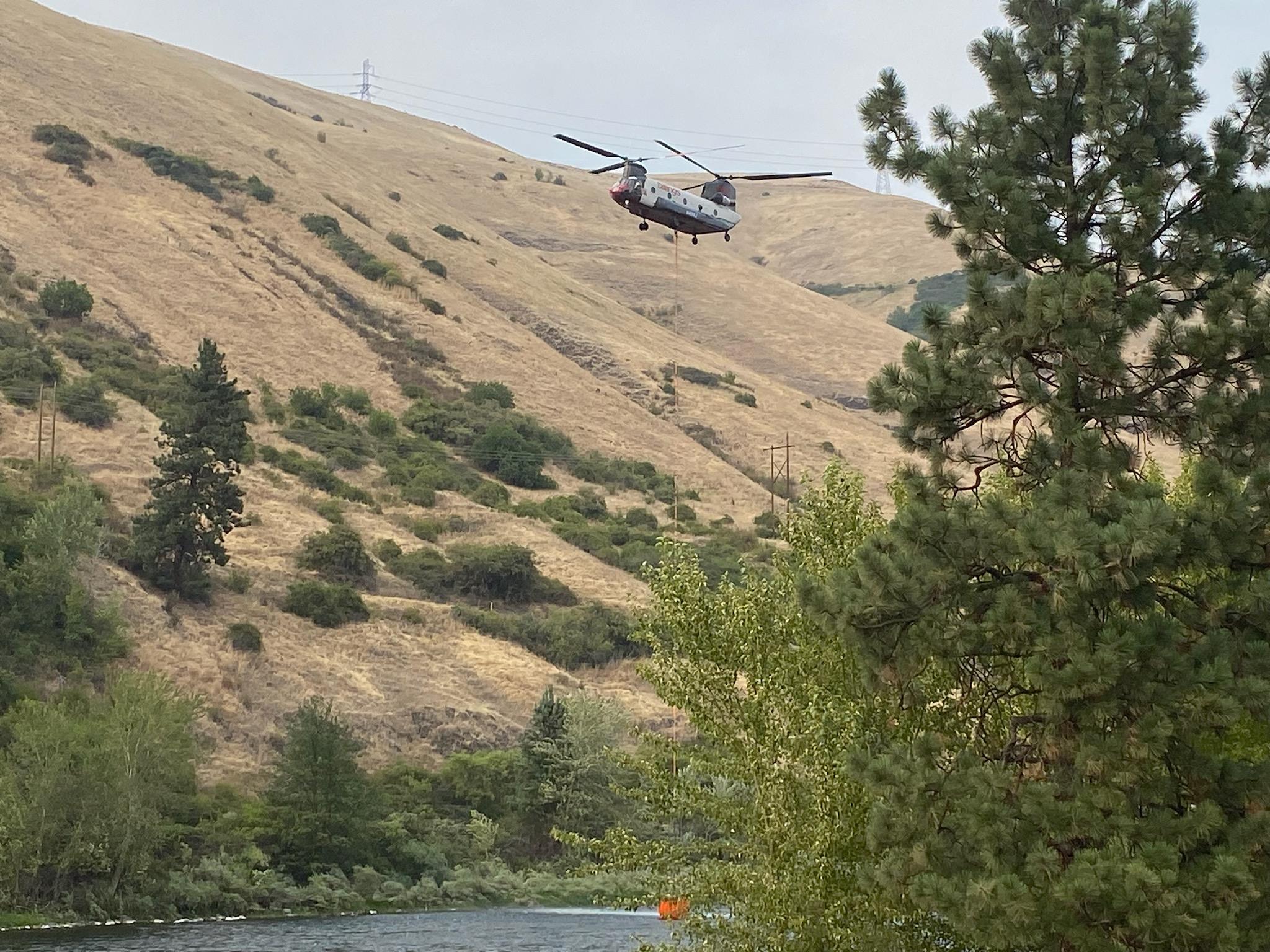 Chinook Helicopter over the river with trees and grassland in the background. 