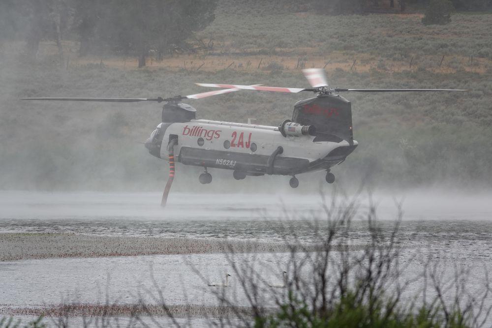 Large twin rotor helicopter hovers above a lake ingesting water with a snorkel