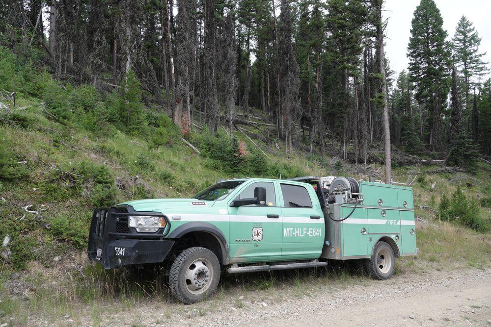 US Forest Service green wildland fire engine parked next to a wooded slope