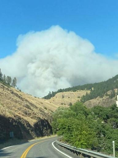 Smoke column from a wildfire coming up behind mountains with a highway in the foreground.