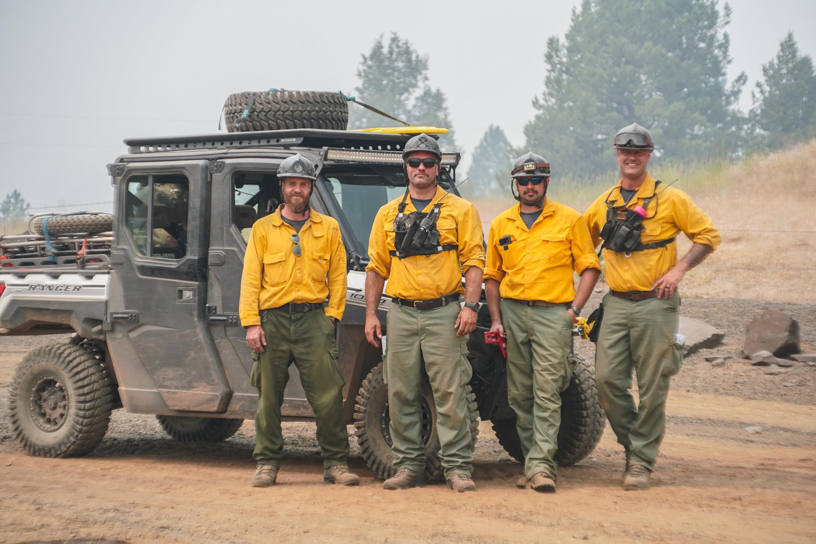 Image of wildland fire medical personnel posing for a photo around a small off-road utility vehicle in a smoky desert landscape. 