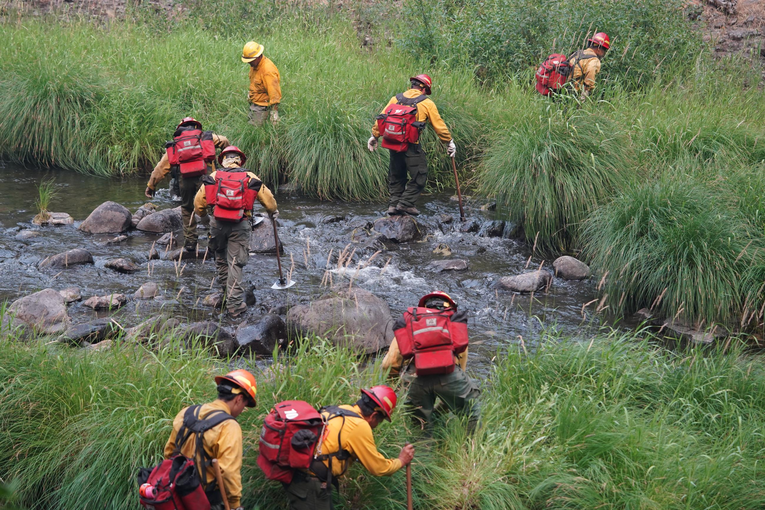 Firefighters crossing a stream with fire gear. 