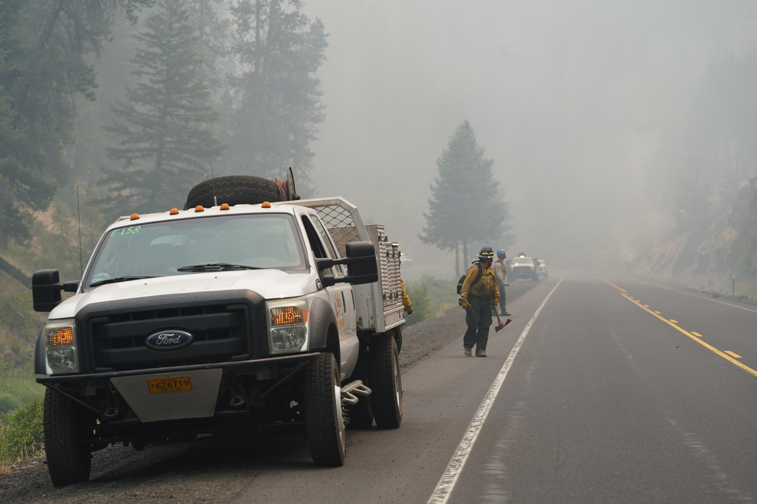 Firefighters on a highway watching a firing operations with an engine on a roadway.